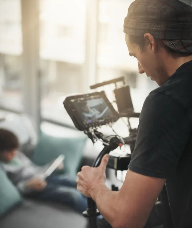 A freelance videographer holding a DSLR video camera on a gimbal in an interior space