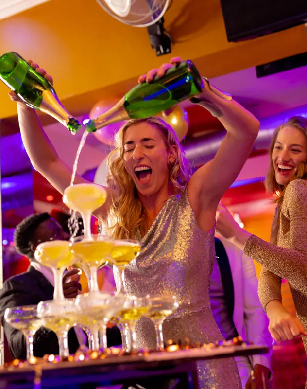 Euphoric woman pouring champagne into a stack of coupe glasses at an event