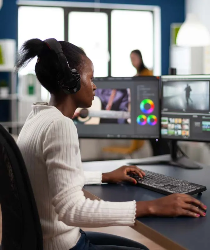 A woman video editing at a desk in a studio with several monitors