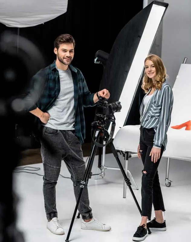 Two people stood in a studio with lights, camera and background 