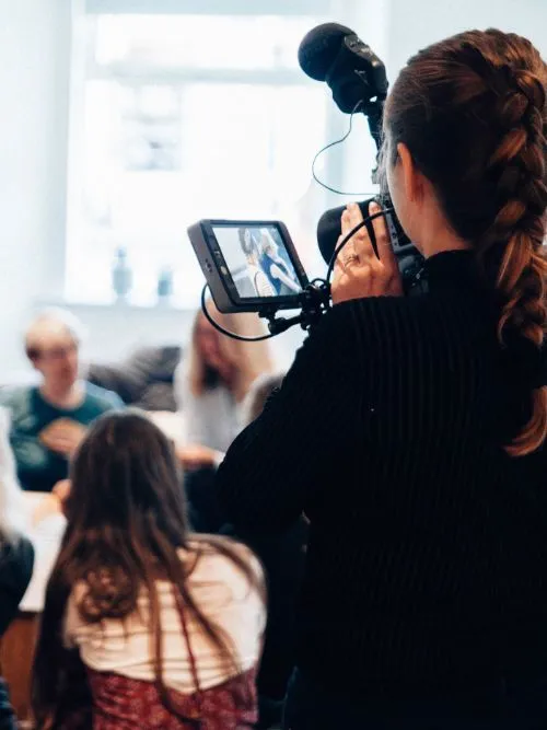 A female videographer with brown hair holding a video camera filming an event