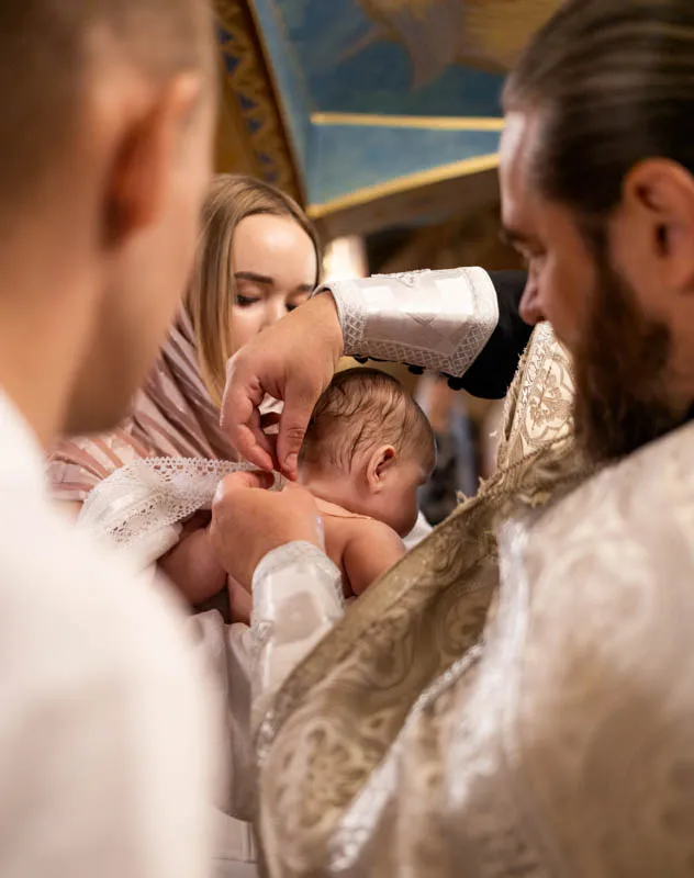 Christening ceremony with priest blessing the back on the baby's head