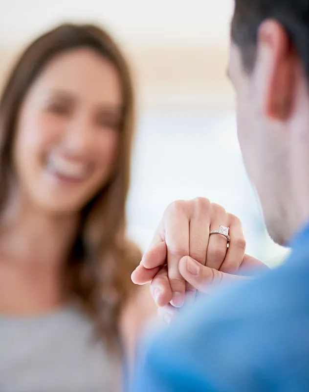 Over the shoulder view of a man holding up an engagement ring to his girlfriend
