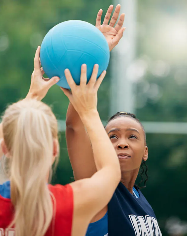 Female netball players on a pitch with the ball about to be thrown mid air