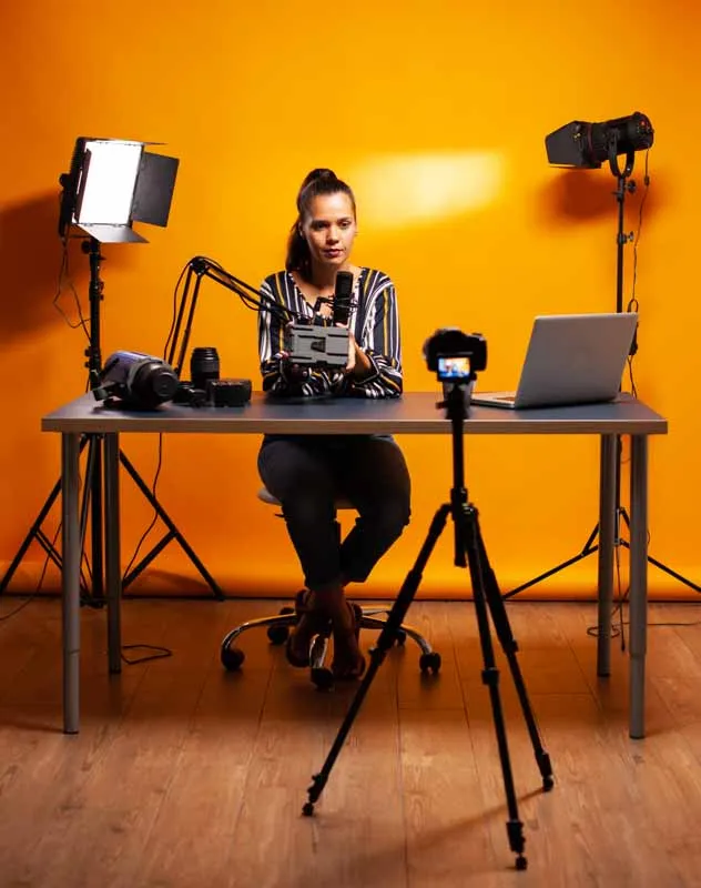 Woman sat at a desk with a portable orange backdrop, camera and lighting