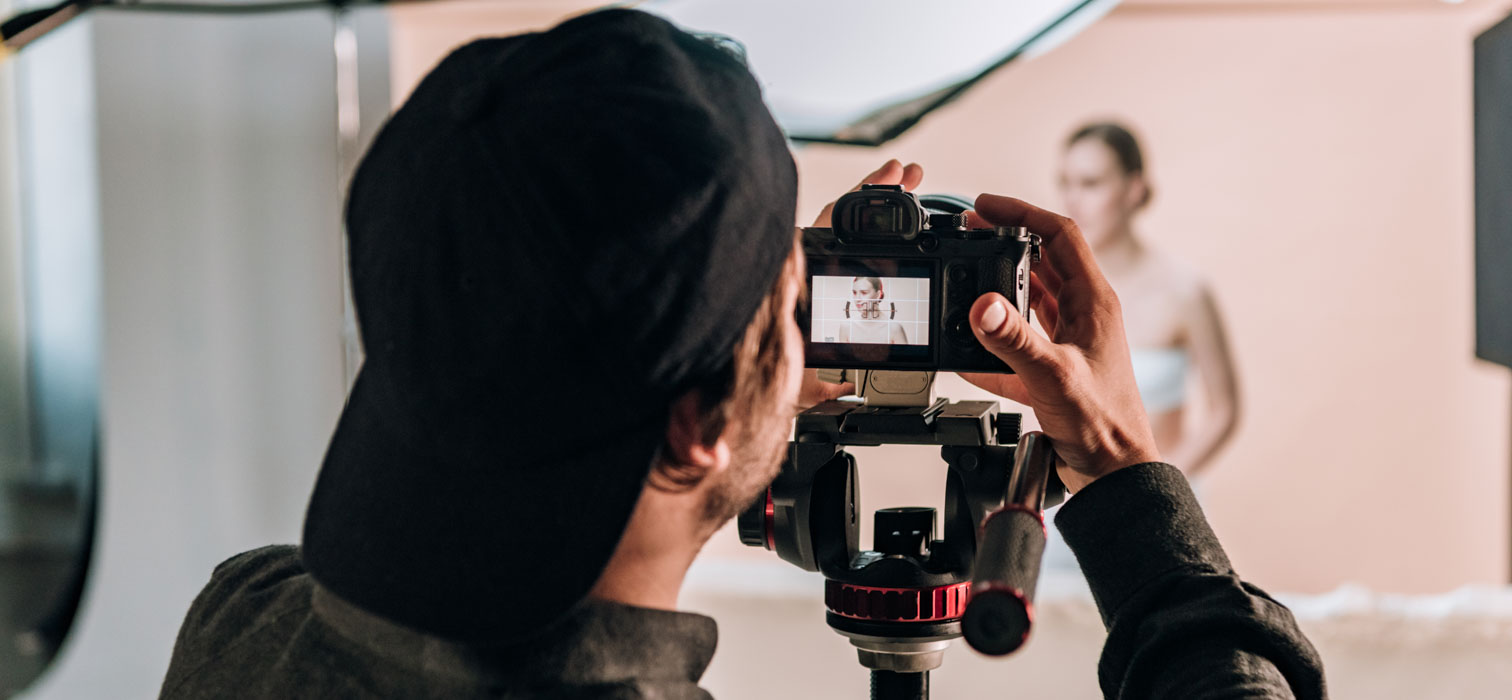 A content creator standing behind a camera filming a female influencer
