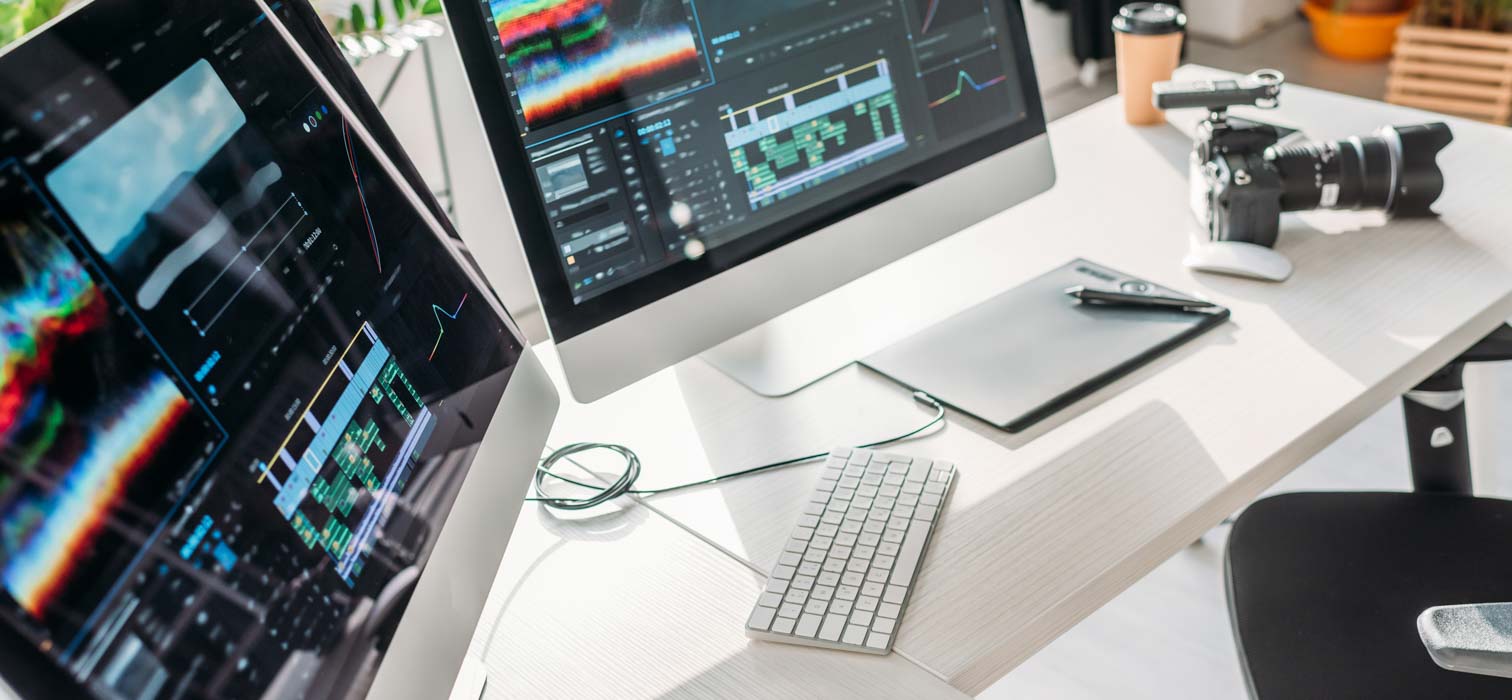 A computer desktop showing two monitors and an Apple keyboard for editing