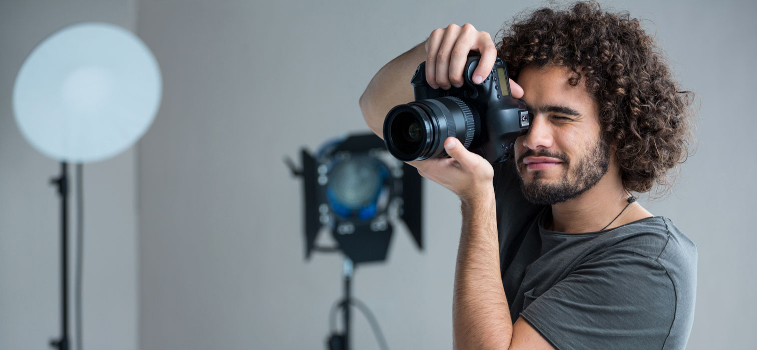 A young male photographer with curly hair point a camera in a studio