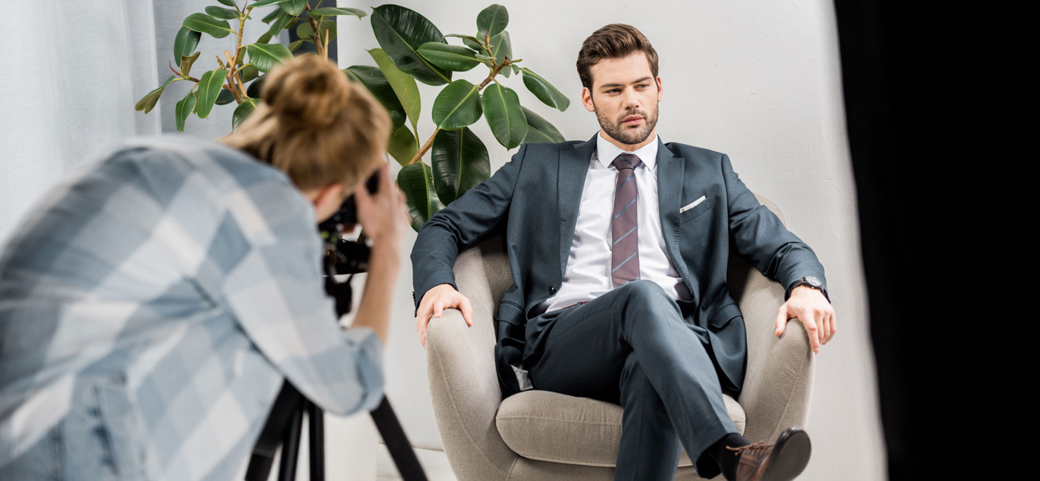 Female photographing a man sat in an office wearing business suit