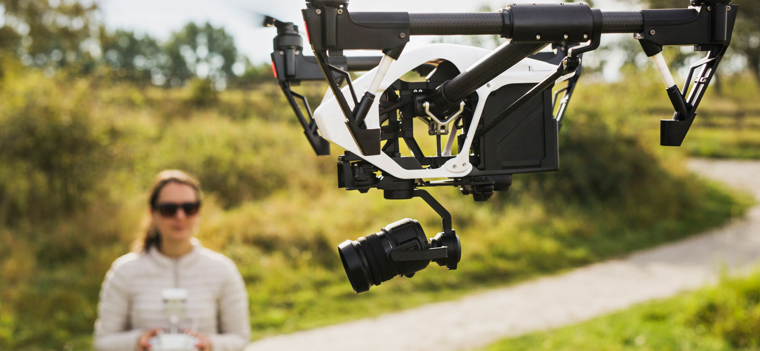 A man in a white shirt standing against holding the controller of a drone seen in foreground