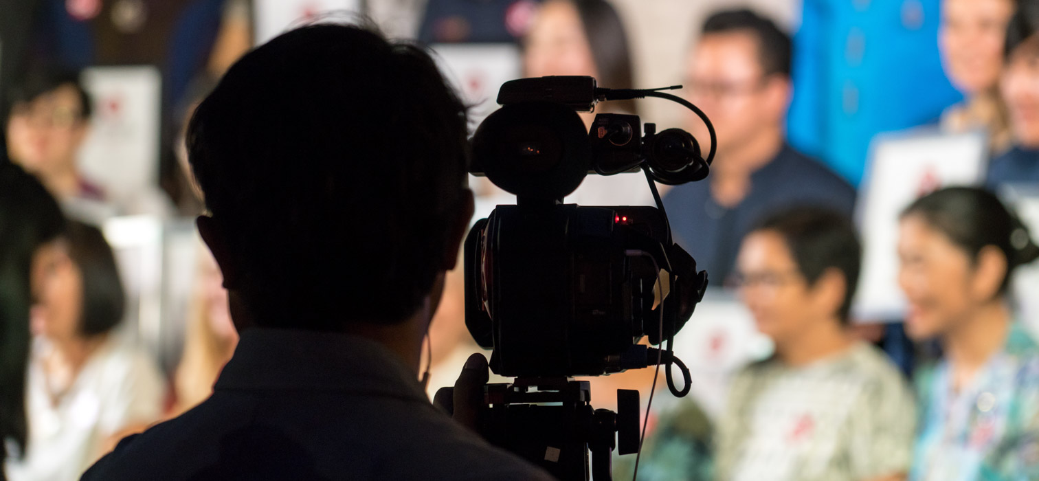 Rear view of a cameraperson seen in silhouette filming the audience at an event