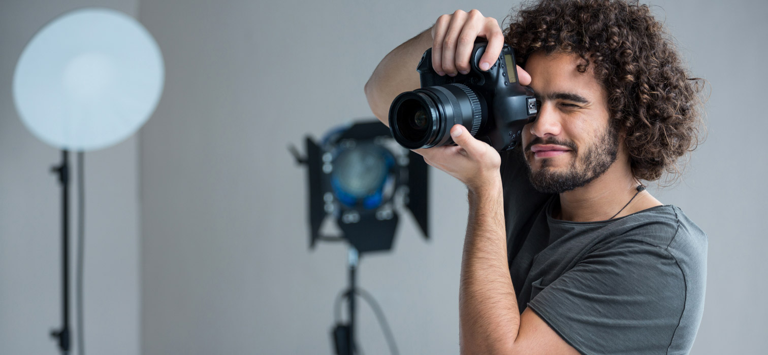 A young male photographer with curly hair point a camera in a studio