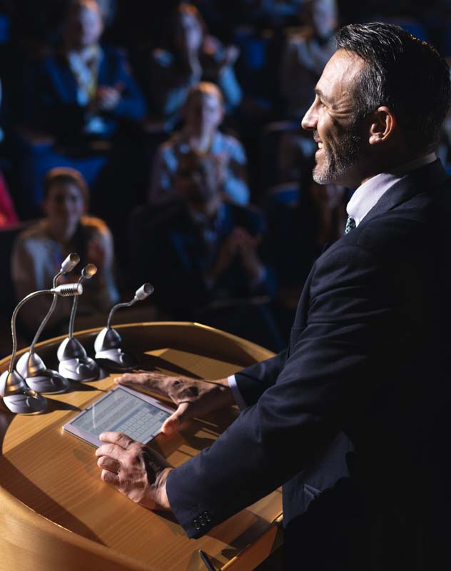 Man standing at a podium address a crowd at a speaker event