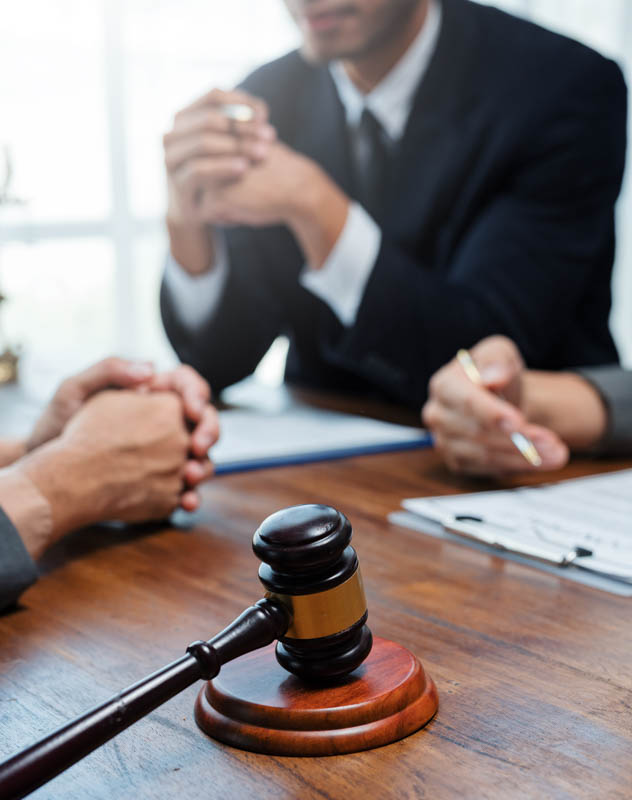 A man in a suit sat in a legal hearing with a gavel in the foreground