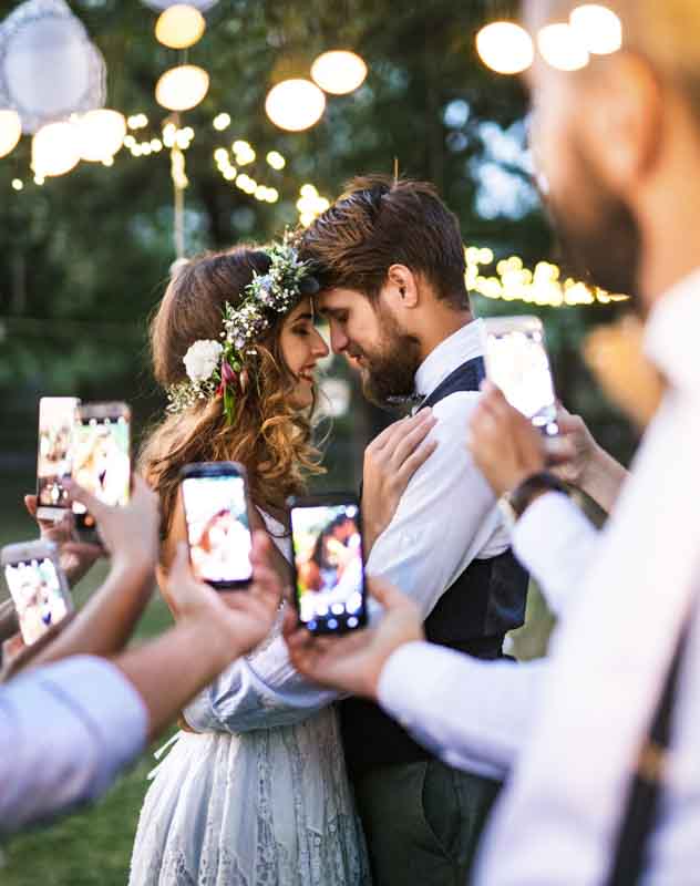 A couple facing each other on the wedding day with people recording on their phones