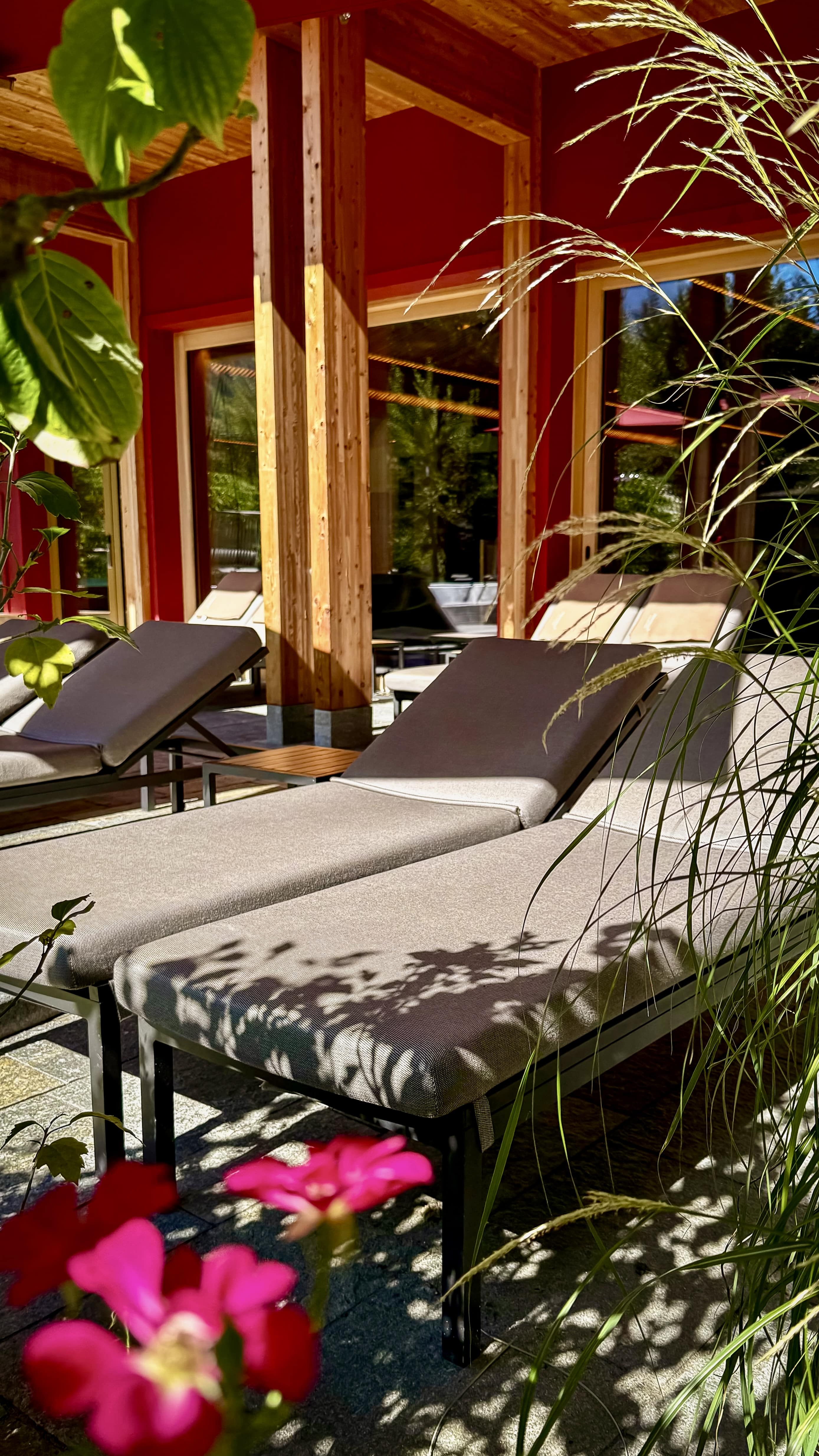 Indoor beige hammock chair with cushions near large glass windows overlooking an outdoor deck with lounge chairs and a mountain landscape.