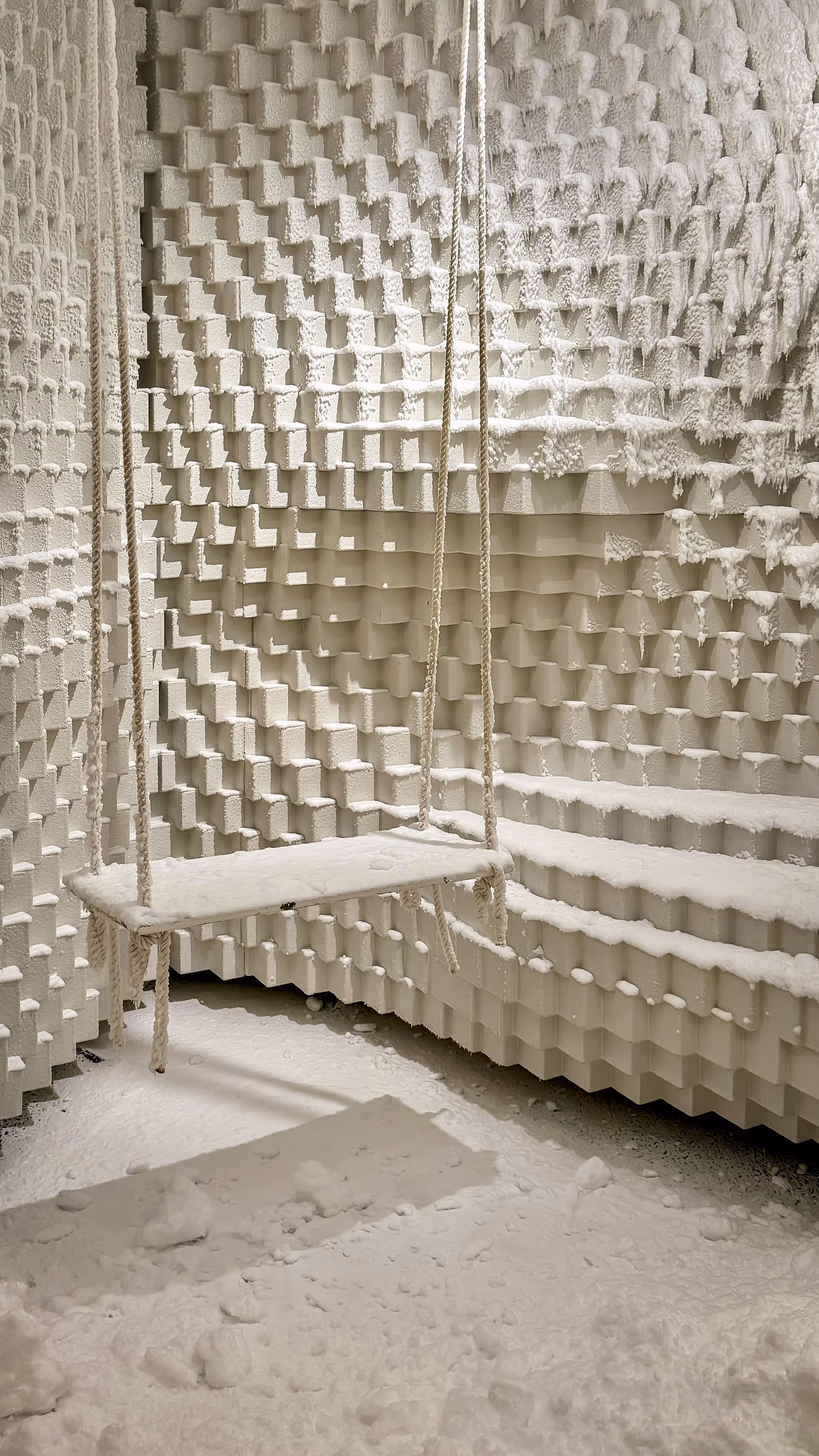 Indoor beige hammock chair with cushions near large glass windows overlooking an outdoor deck with lounge chairs and a mountain landscape.