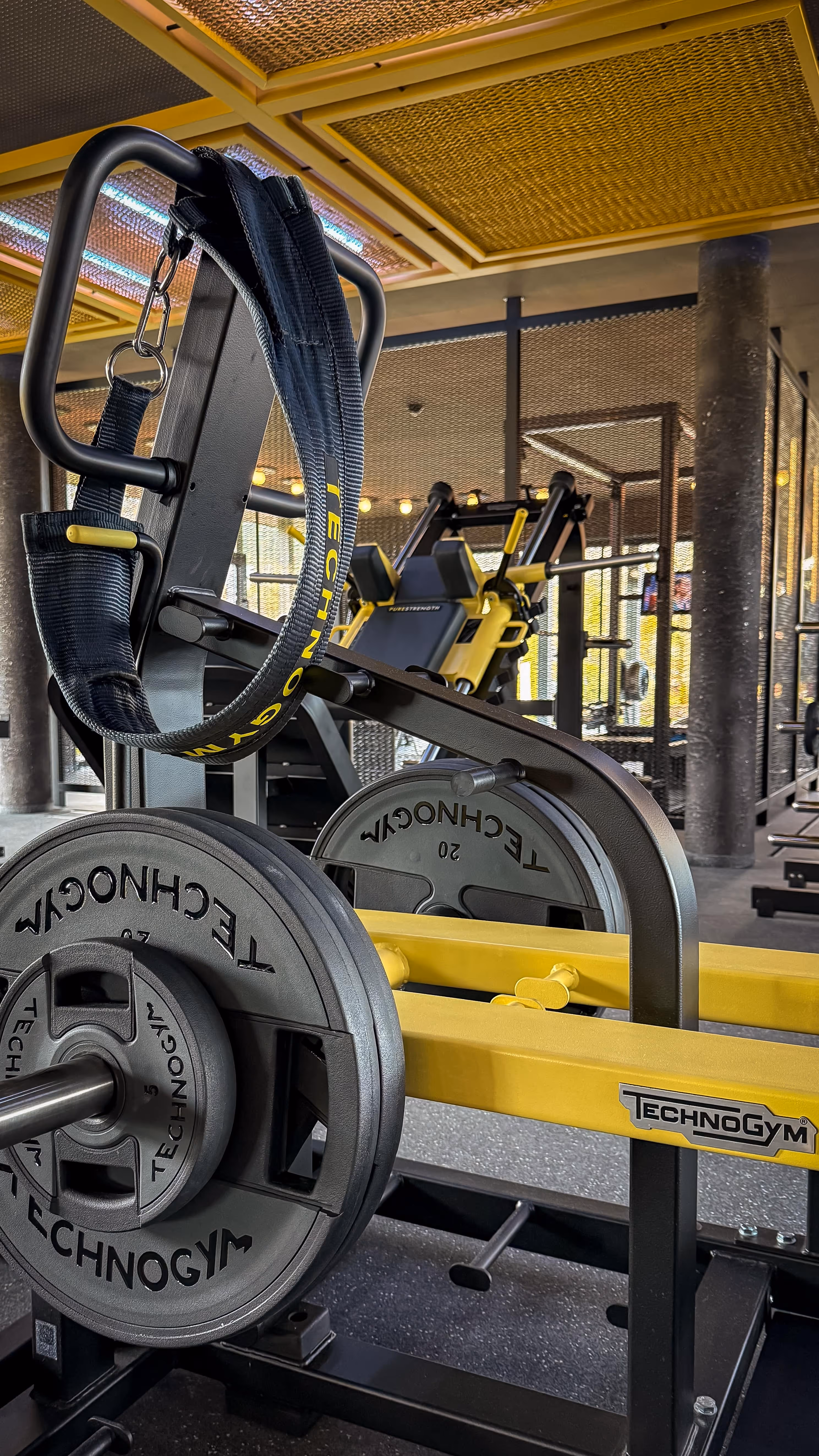 Modern Pilates reformer machine with wood frame and padded platform in a bright studio with wooden floor and dark textured wall.
