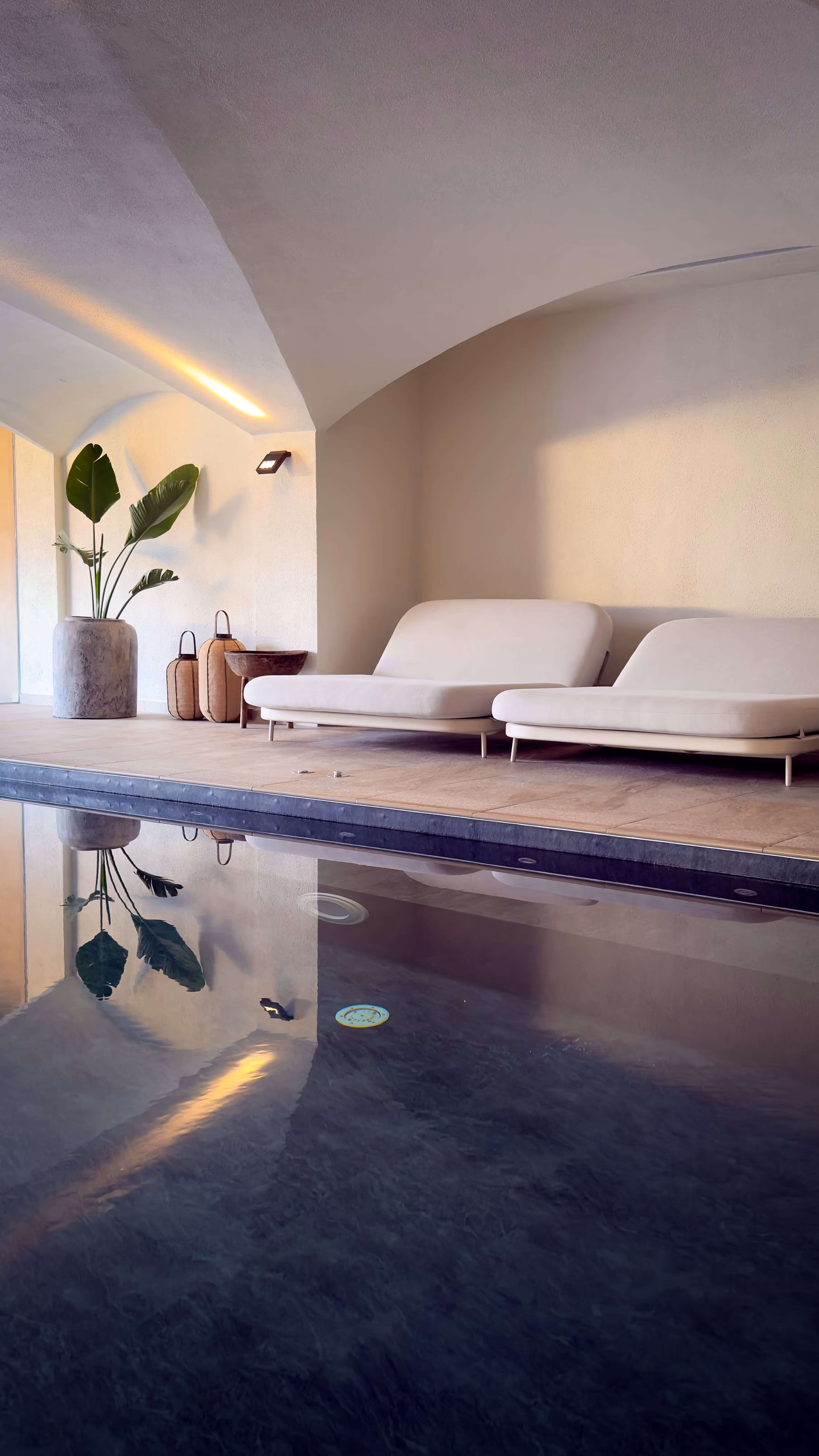 Clear natural swimming pool with lounge chairs and a mountain backdrop under a blue sky.