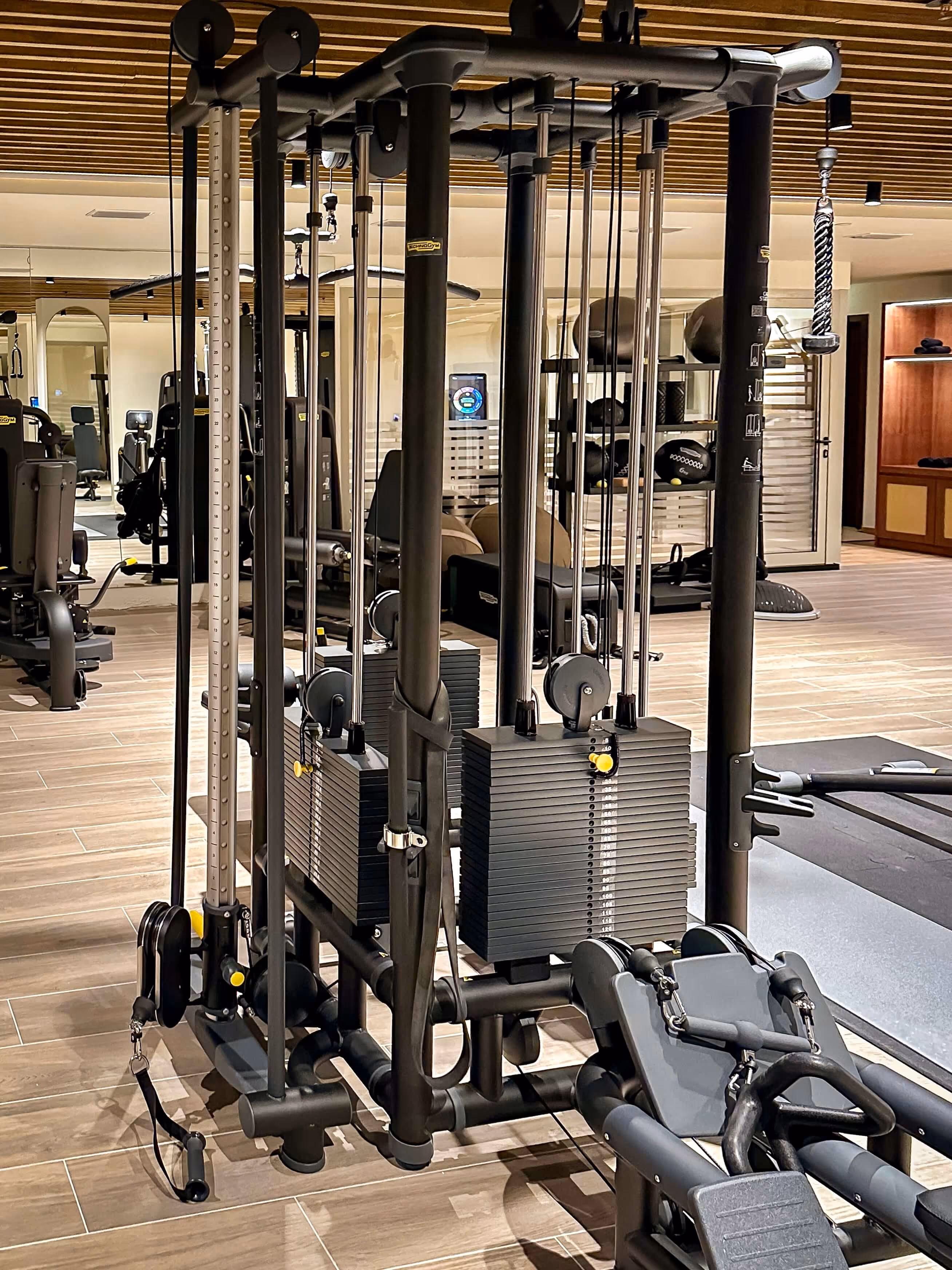 Sunlit sauna interior with wooden benches and folded white towels, with a glass door offering a view of mountains and buildings outside.