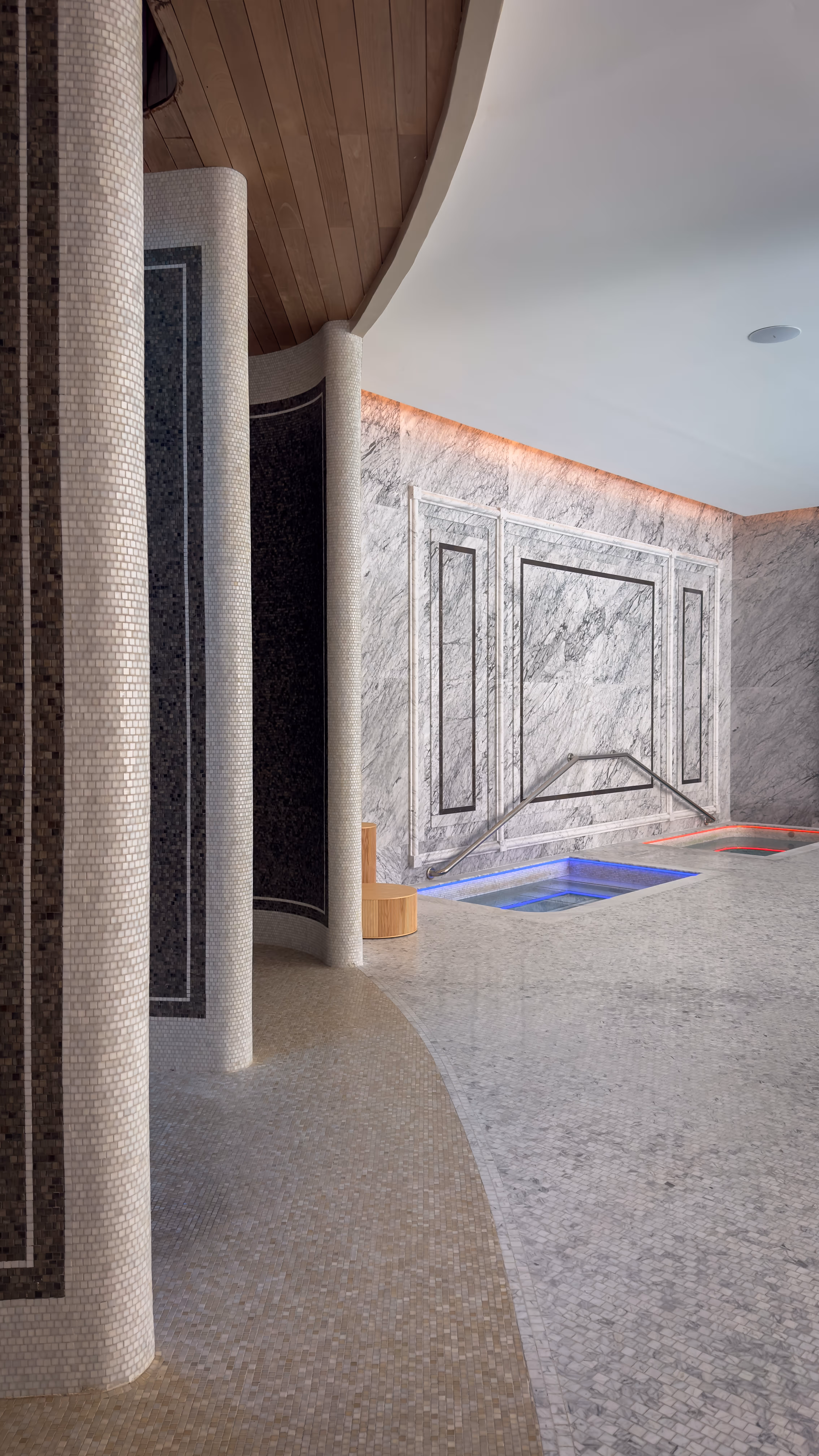 Clear natural swimming pool with lounge chairs and a mountain backdrop under a blue sky.