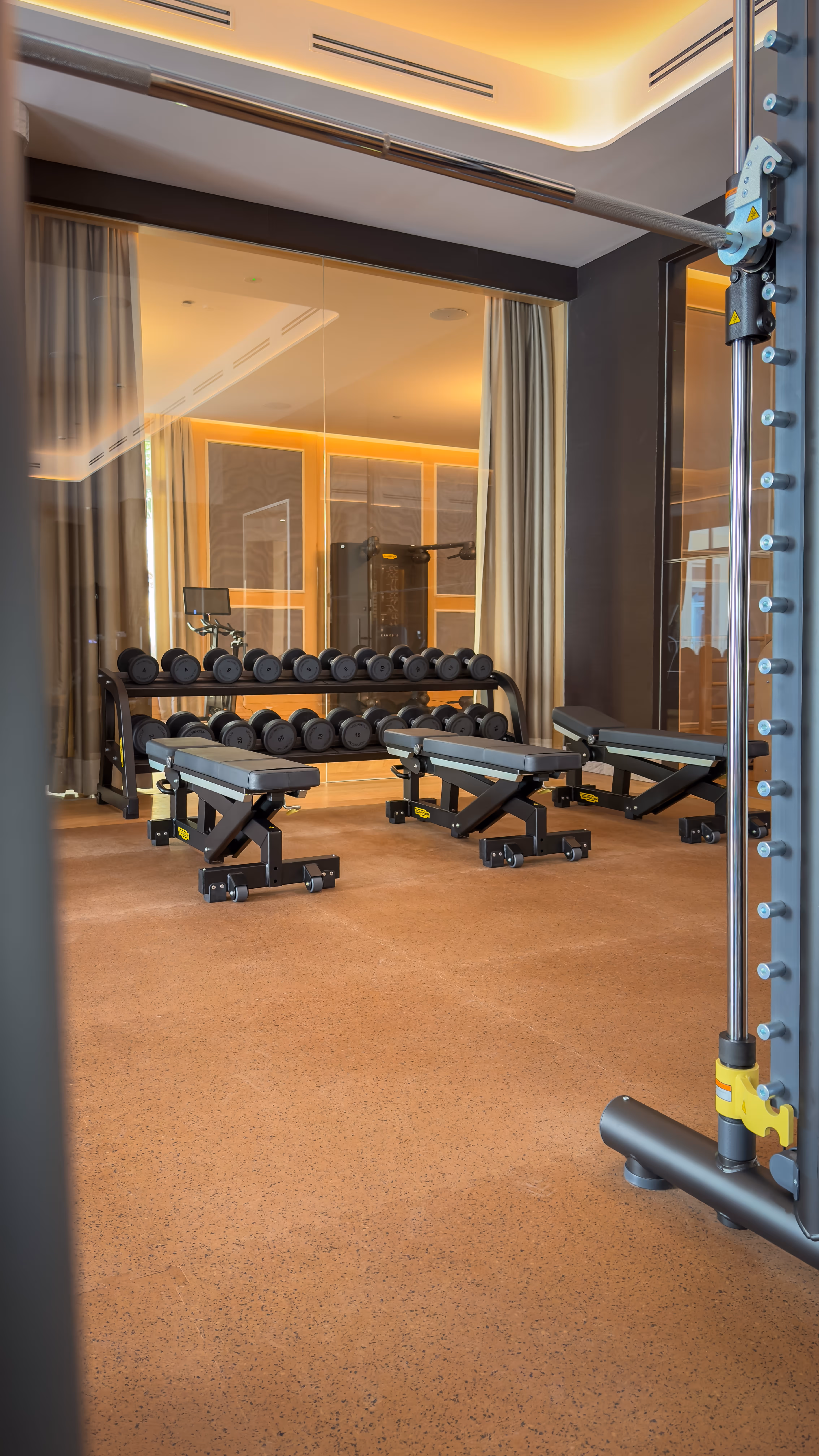 Modern Pilates reformer machine with wood frame and padded platform in a bright studio with wooden floor and dark textured wall.