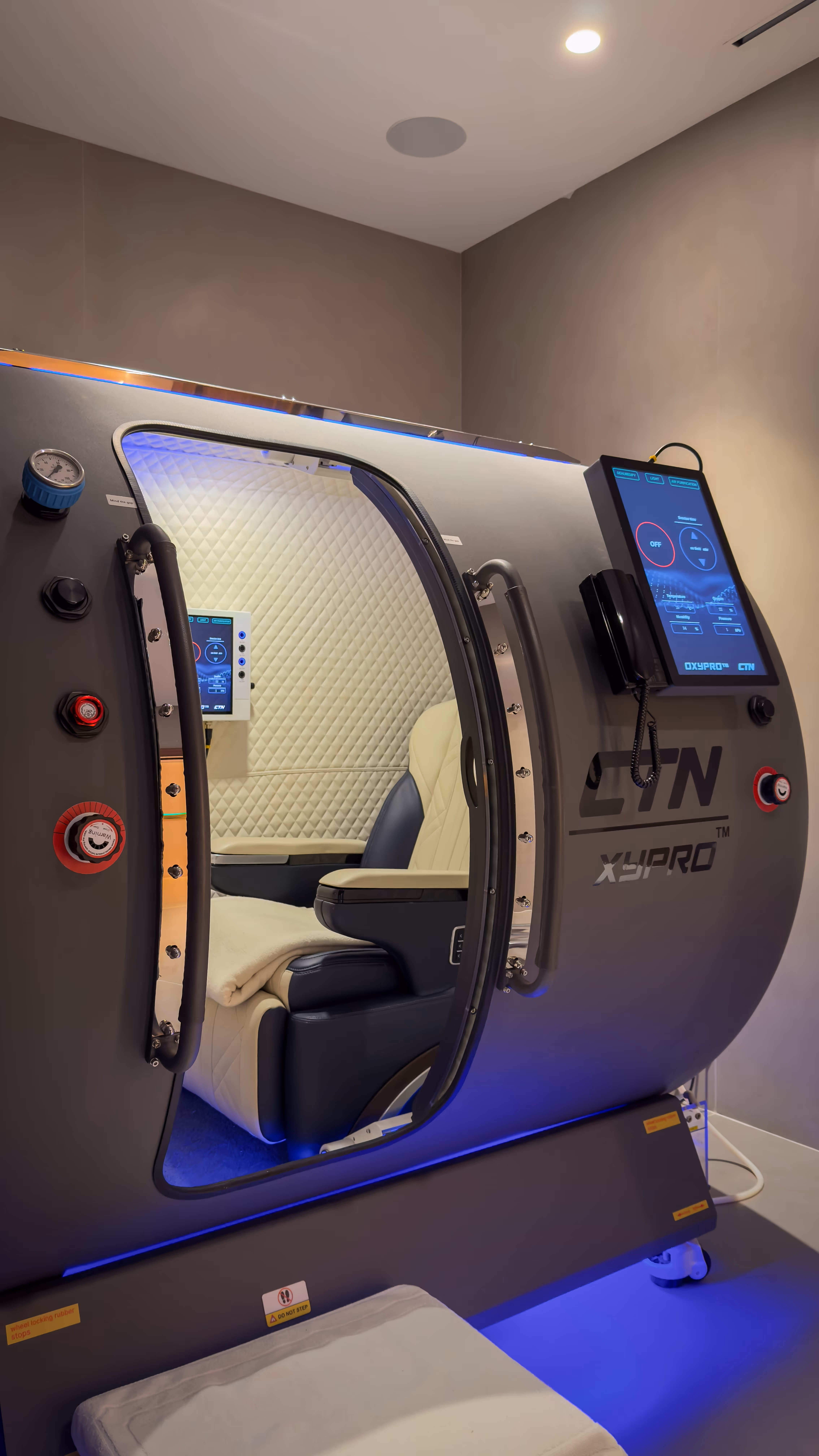 Sunlit sauna interior with wooden benches and folded white towels, with a glass door offering a view of mountains and buildings outside.