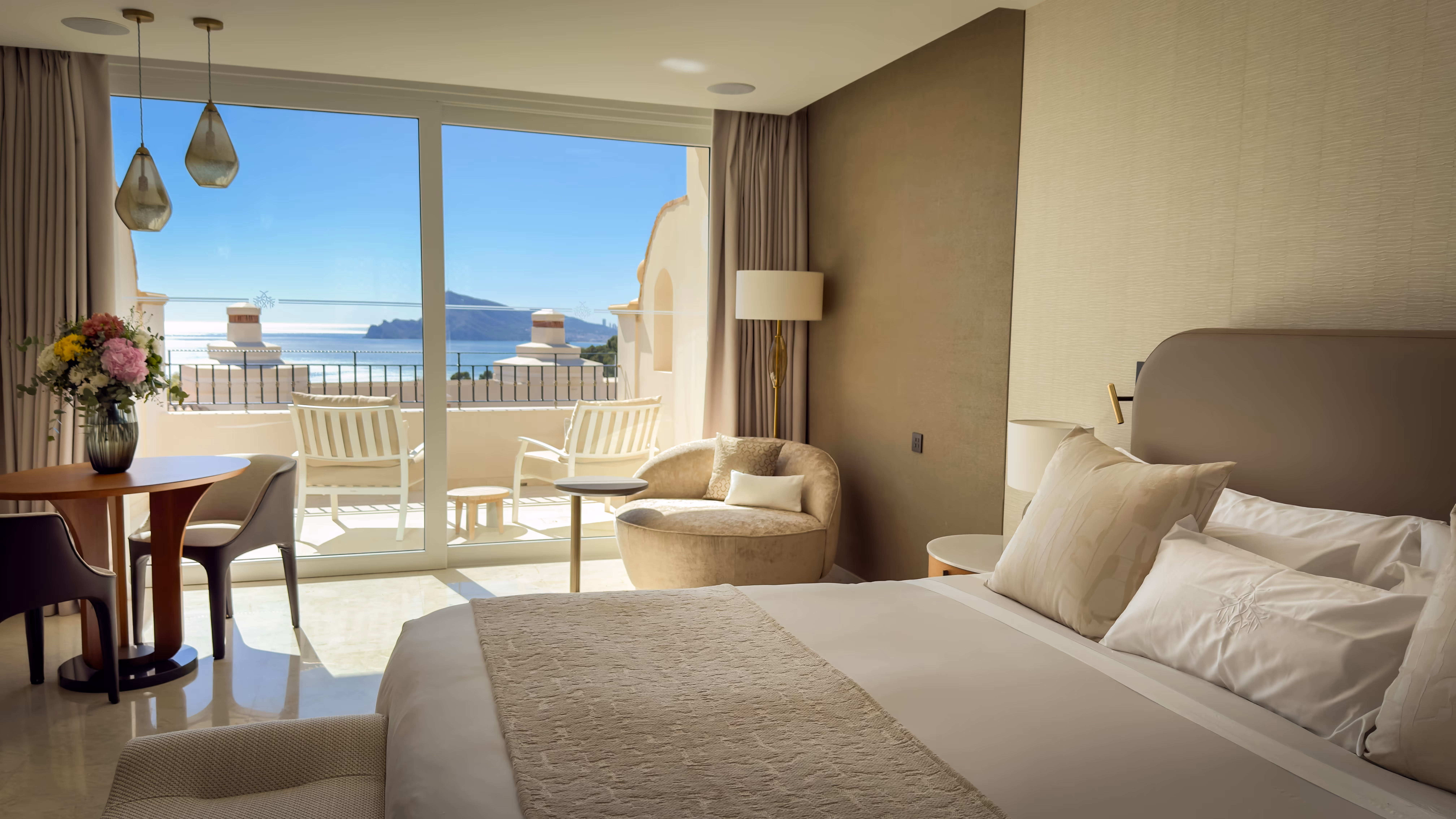 Outdoor pool beside green lawn with red flowering bushes, lounge chairs, and mountainous forest background under clear blue sky.