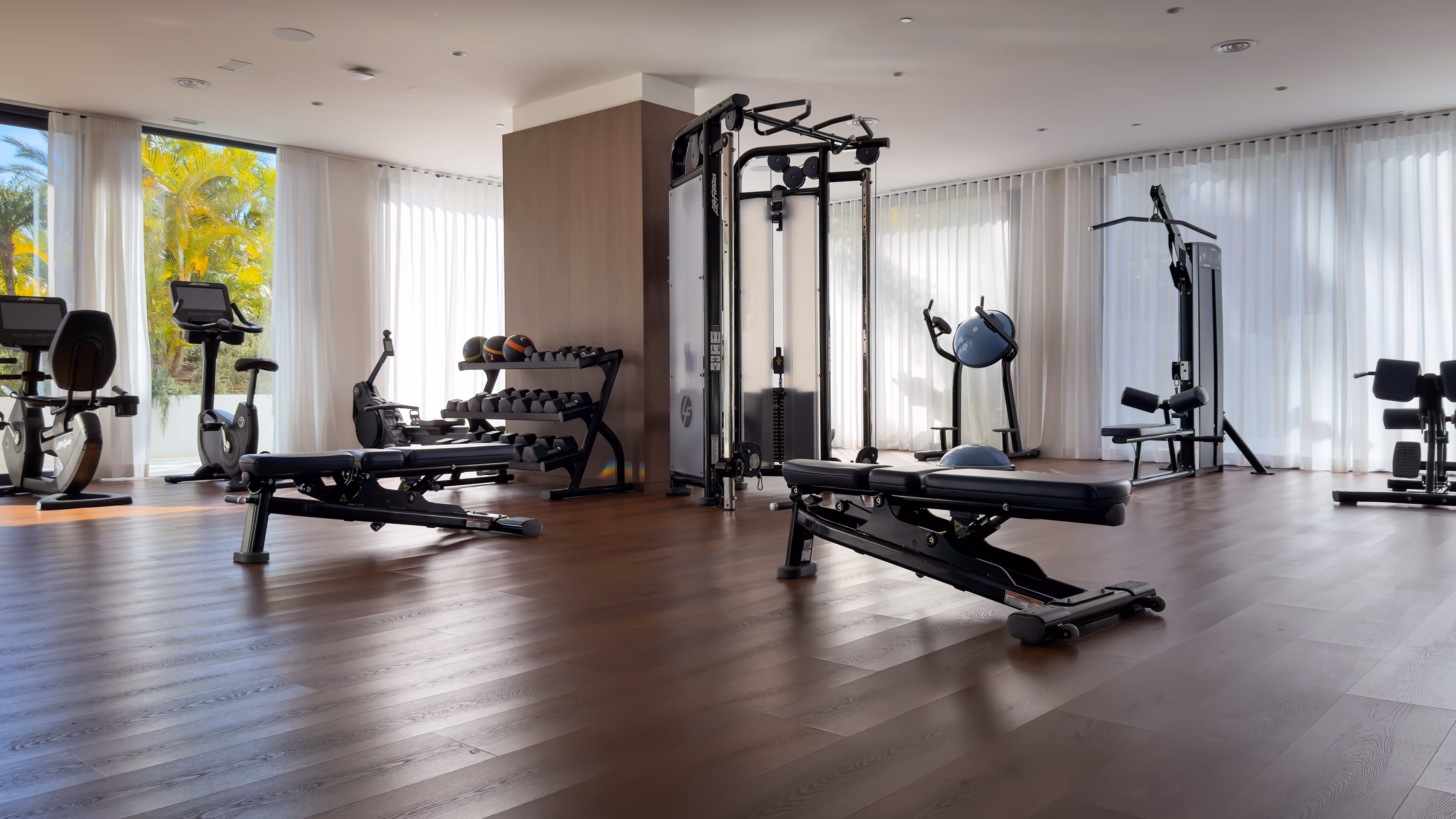 Bright modern gym with exercise bikes, weight benches, medicine balls, and strength training machines.