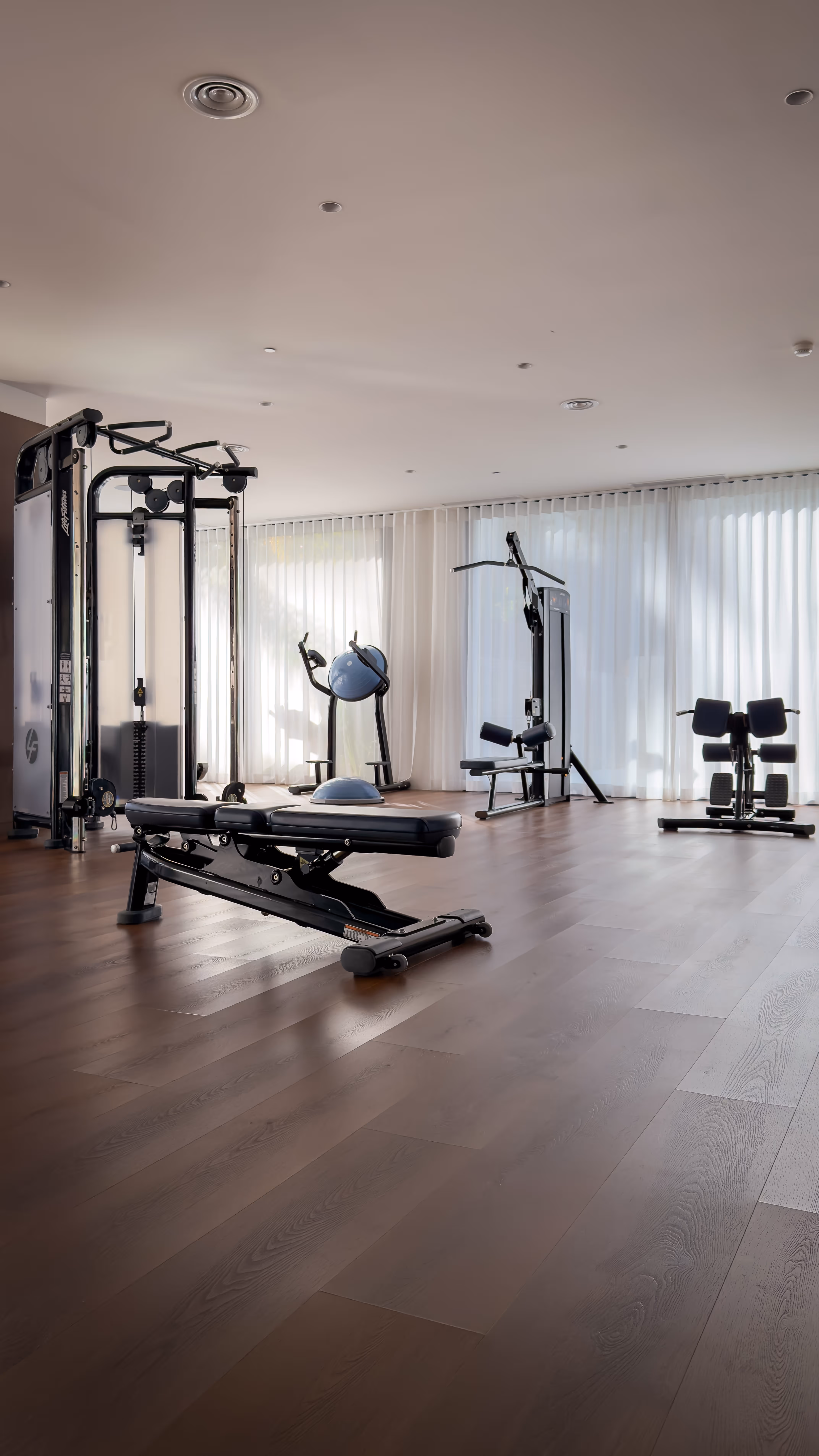 Sunlit sauna interior with wooden benches and folded white towels, with a glass door offering a view of mountains and buildings outside.