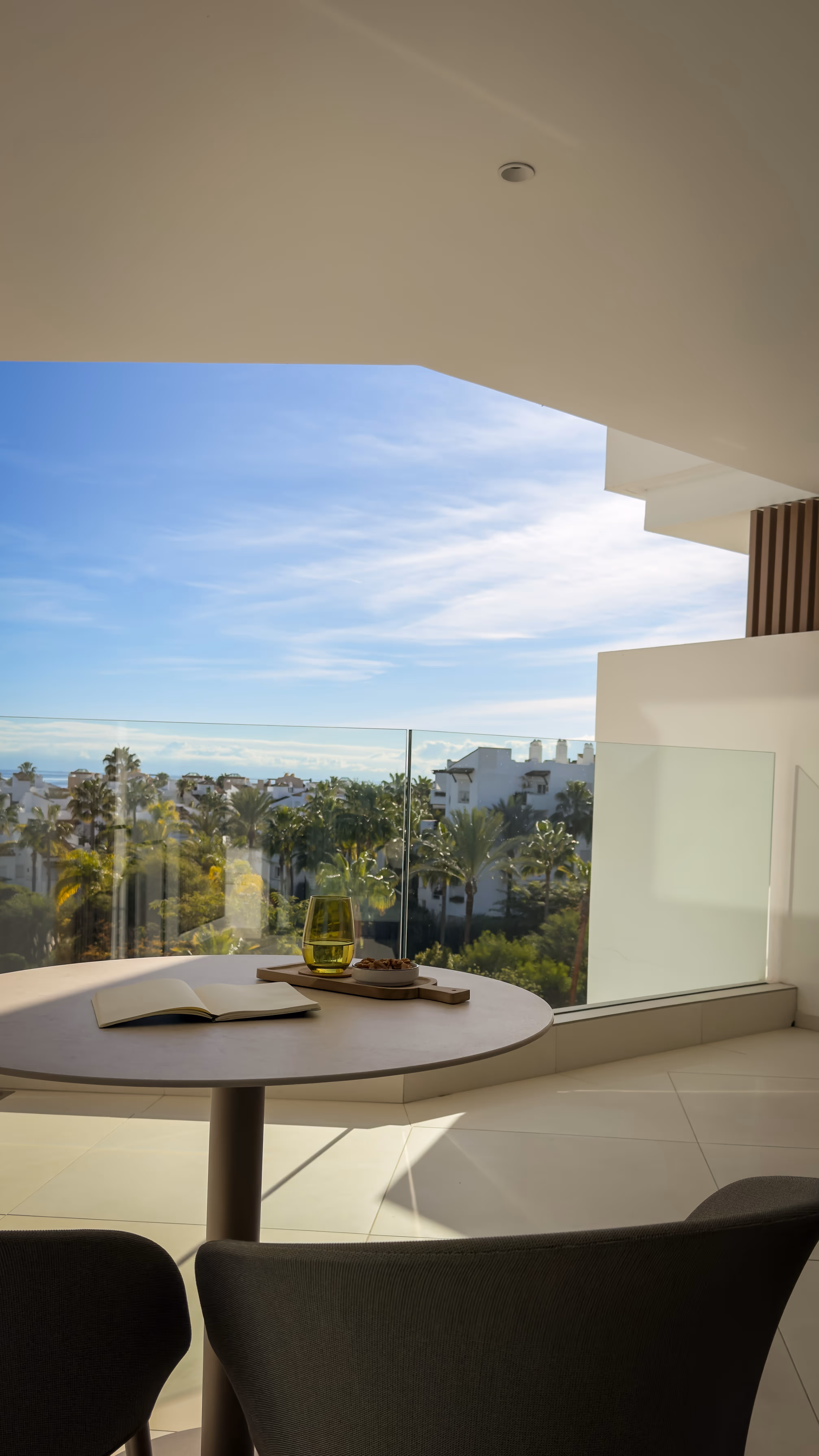 Clear natural pond with plants and a wooden cabin in the background, snow-capped mountains under a blue sky.