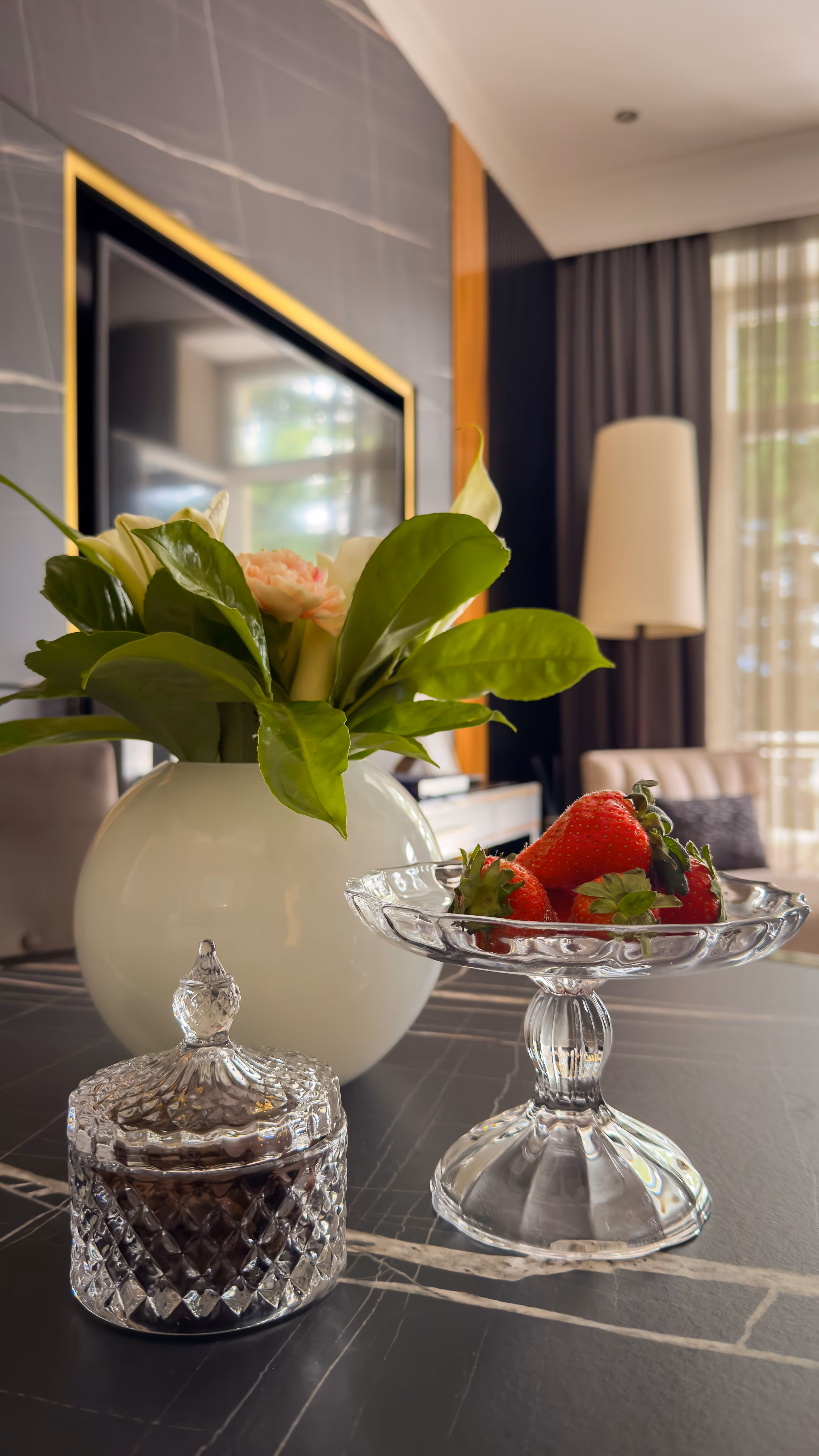 Glass jar, crystal dessert dish with strawberries, and white vase with green leaves on table.