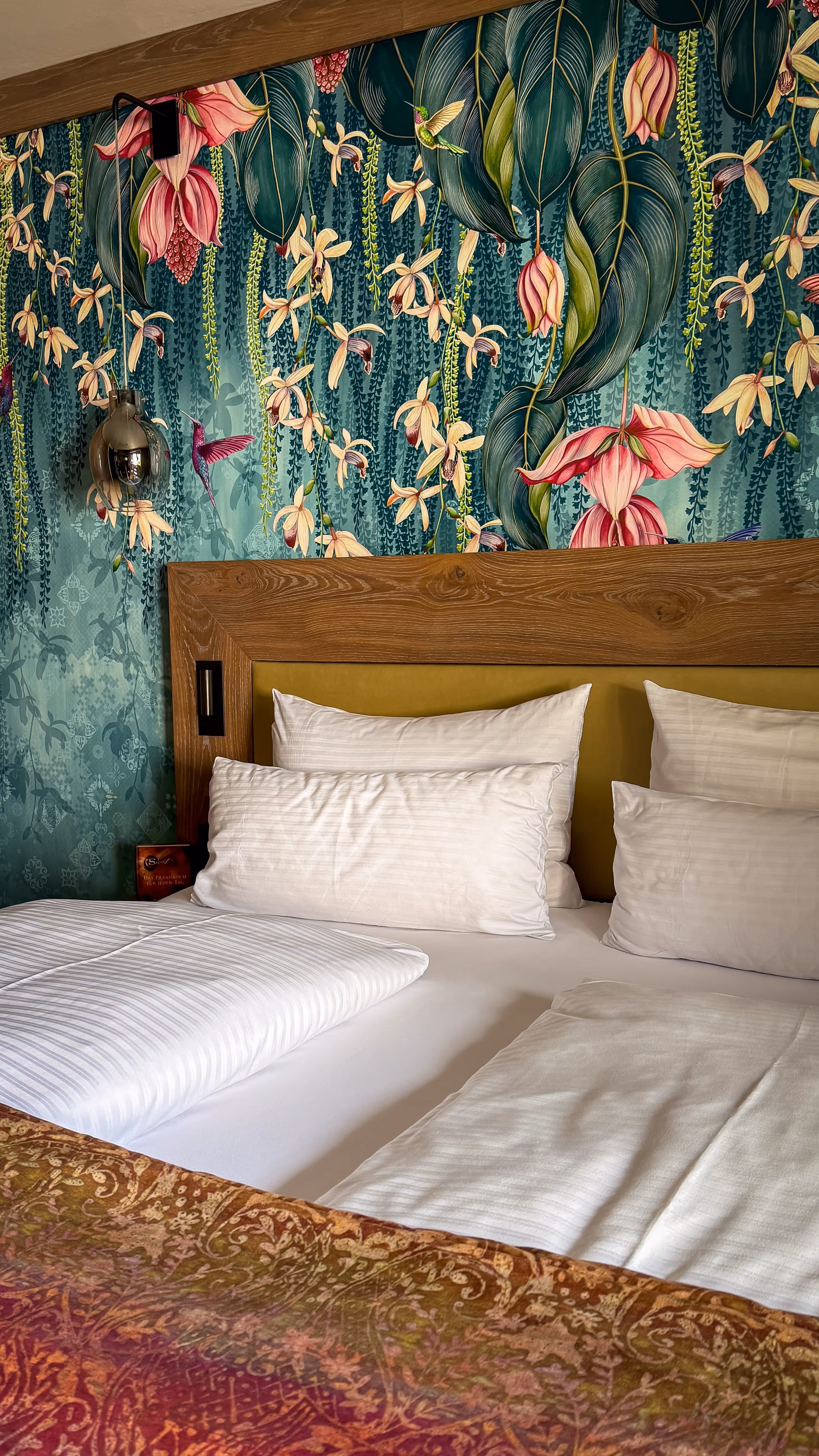 Bed with white pillows and bedding against a vibrant floral and hummingbird wallpaper backdrop.