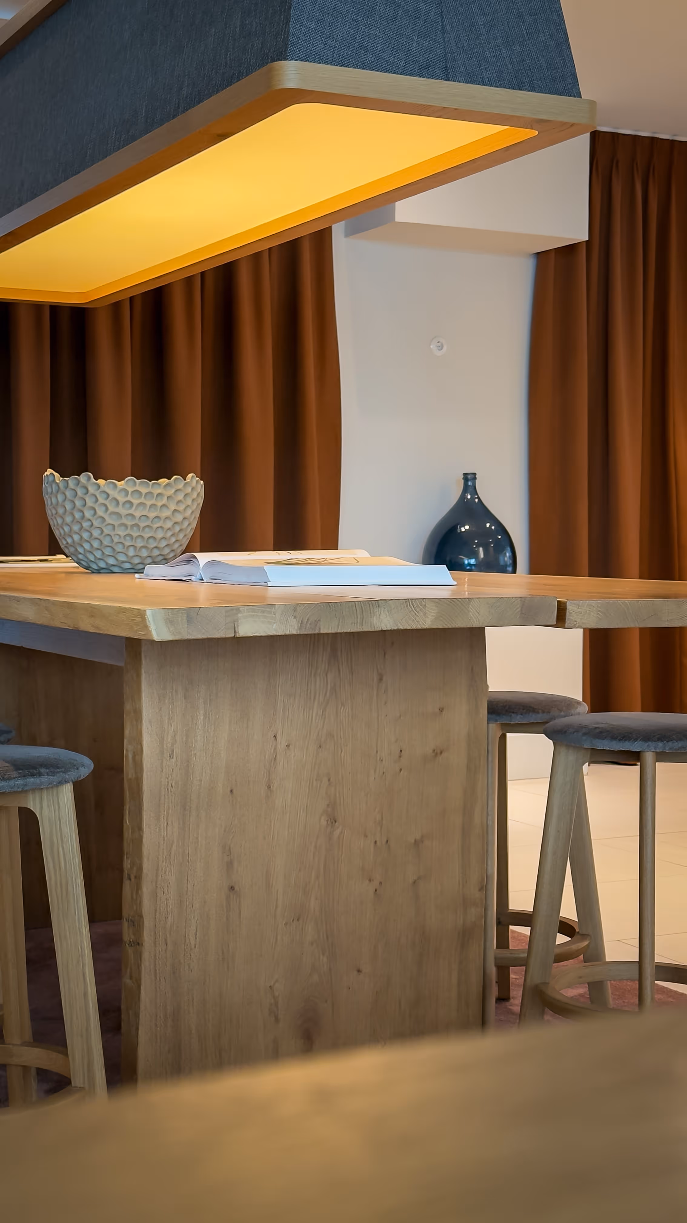 Wooden dining table with stools, a textured bowl, open book, and warm overhead light.