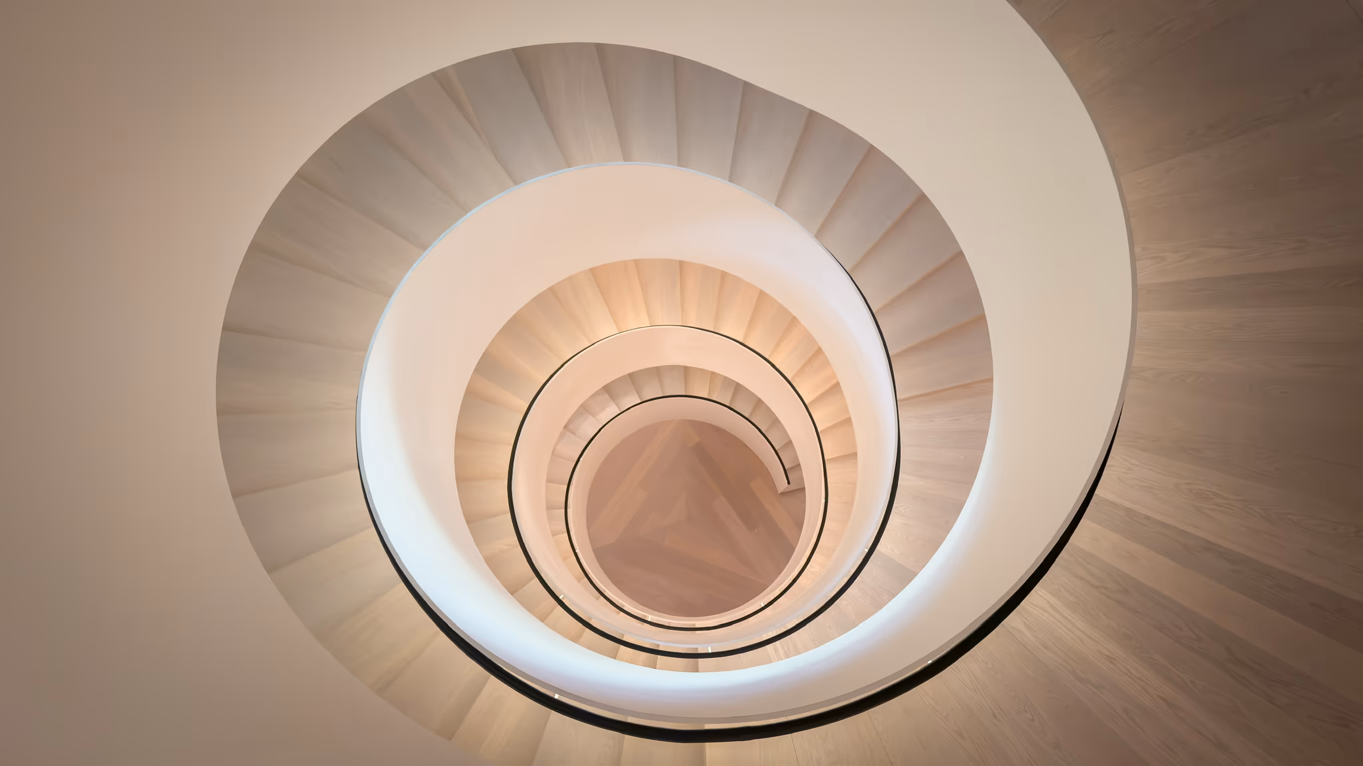 Top-down view of a spiral staircase with beige steps and curved white handrails.
