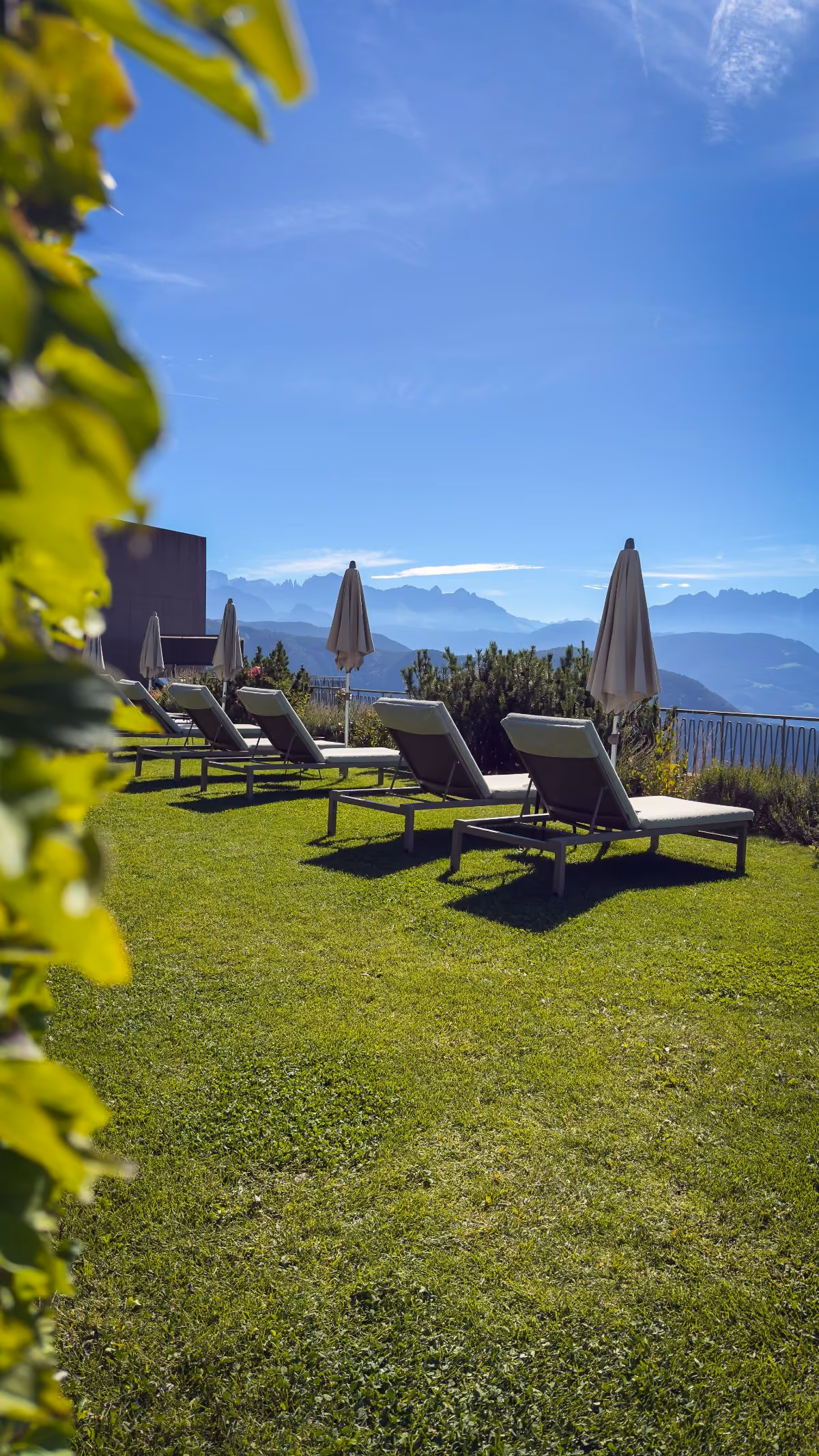 Clear natural swimming pond with lounge chairs and wooden decks, mountains and blue sky in the background.