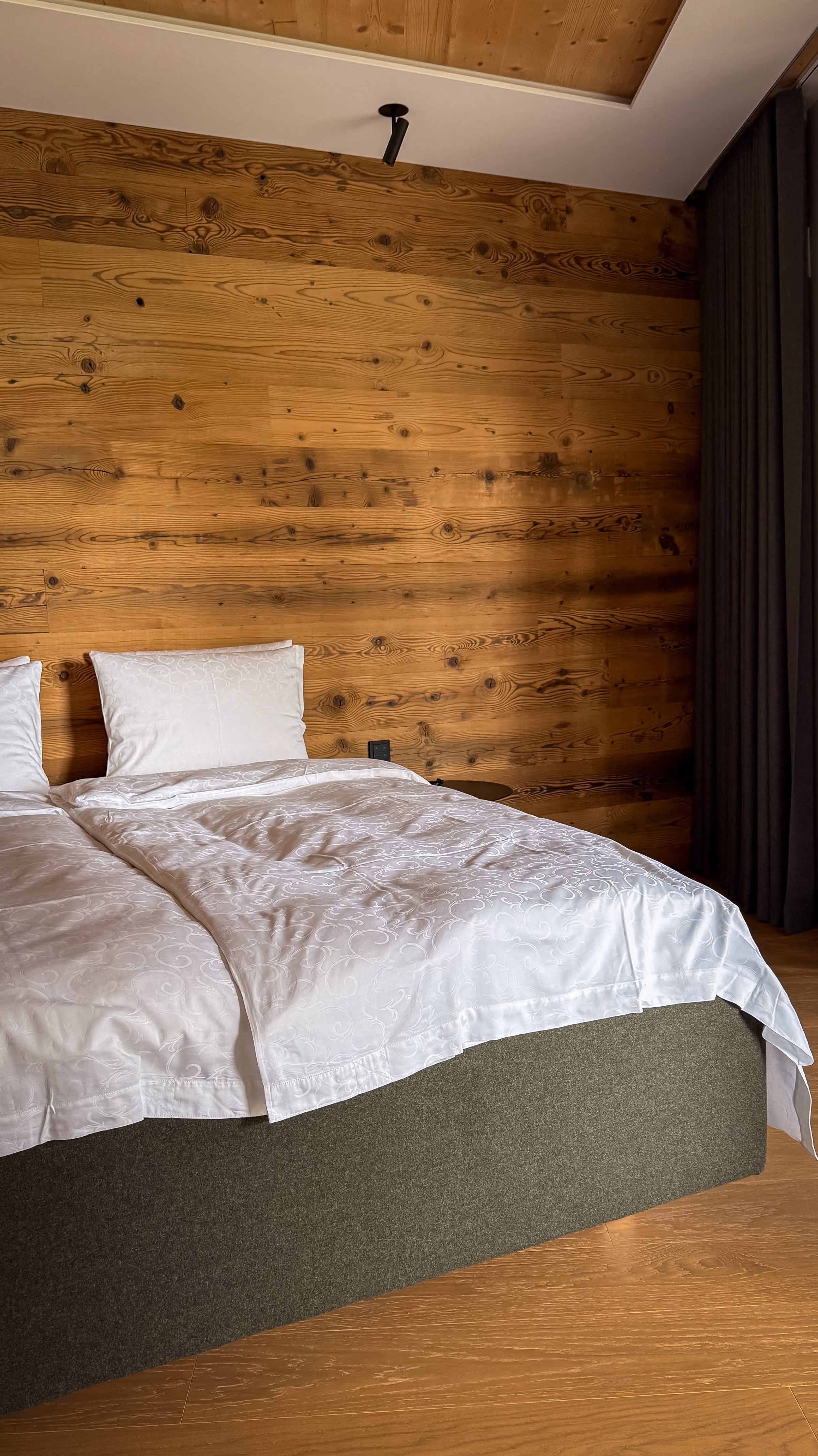 A neatly made bed with white linens and a pillow against a wooden wall with natural knots and grain.