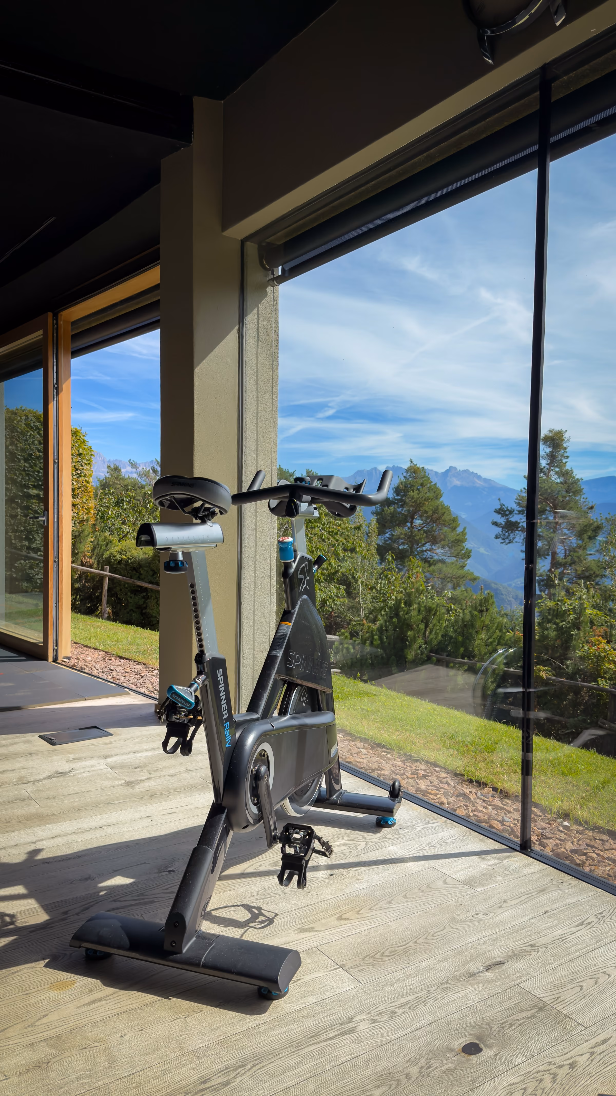 A modern restaurant interior with neatly set dining tables featuring glassware, napkins, and cutlery, large windows offering a view of mountains and outdoor seating with umbrellas under a clear sky.