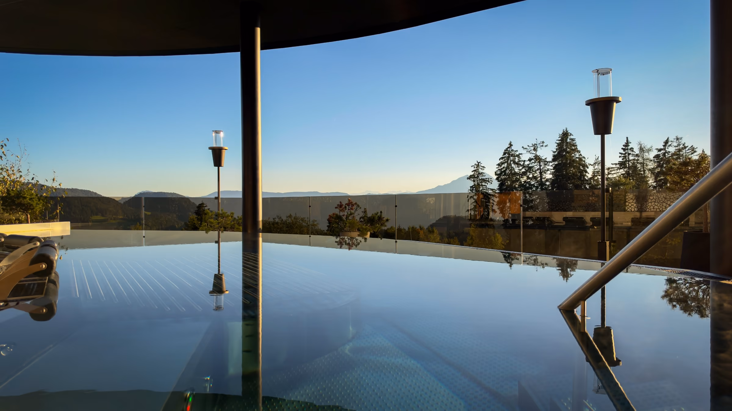 A modern restaurant interior with neatly set dining tables featuring glassware, napkins, and cutlery, large windows offering a view of mountains and outdoor seating with umbrellas under a clear sky.