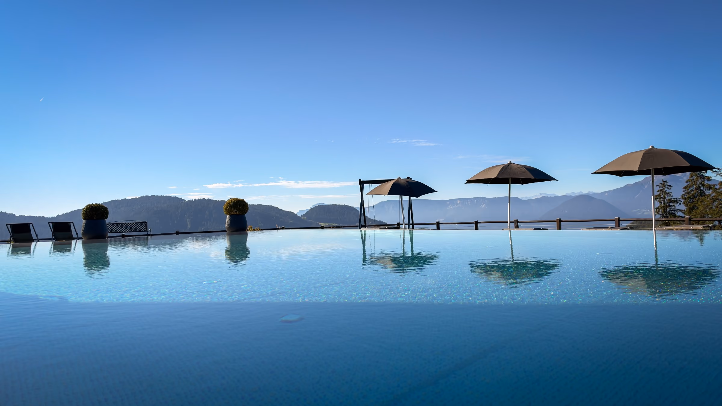 Clear natural swimming pond with lounge chairs and wooden decks, mountains and blue sky in the background.