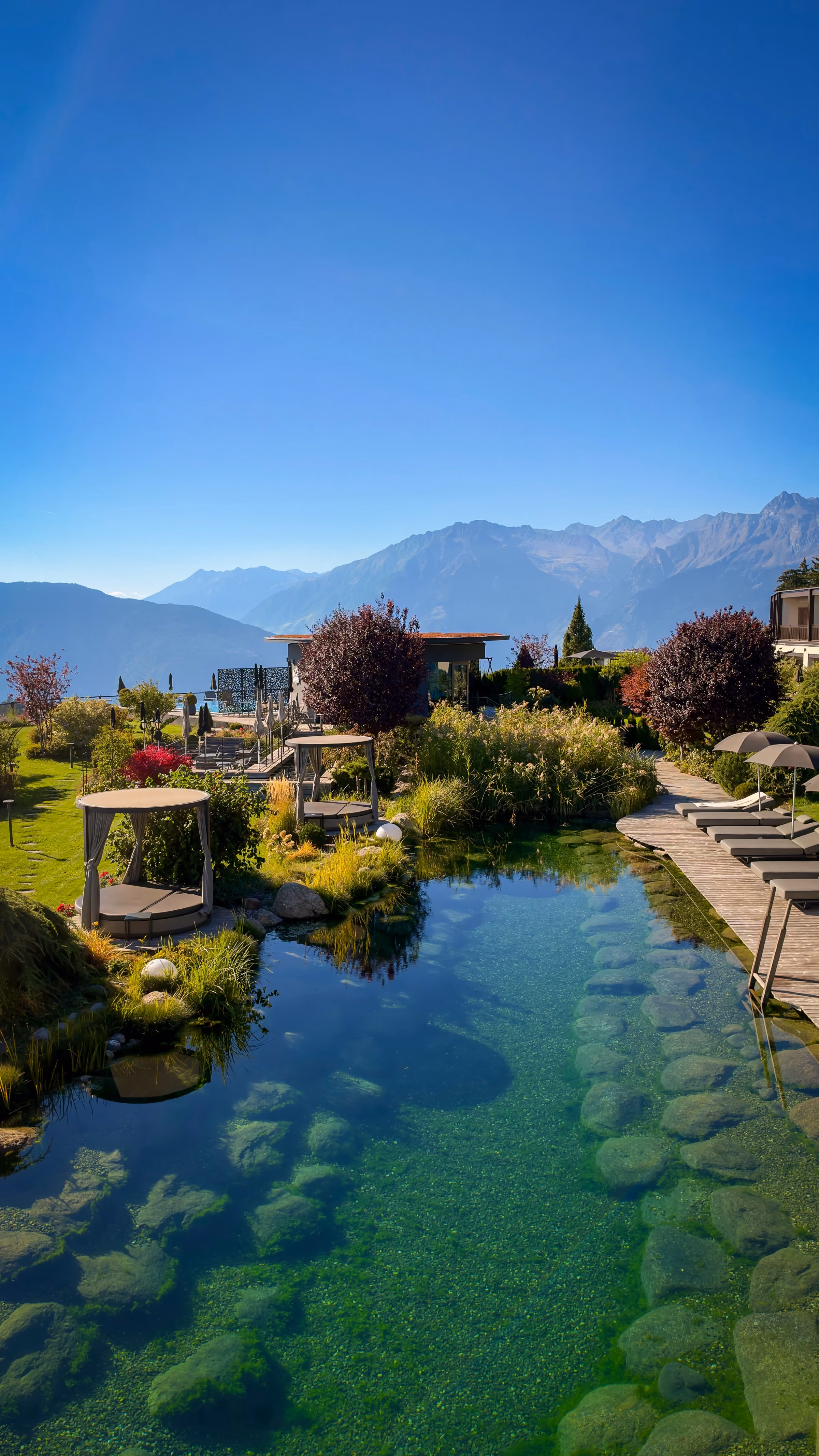 Infinity pool overlooking a forested mountain range with layered peaks under a partly cloudy blue sky.