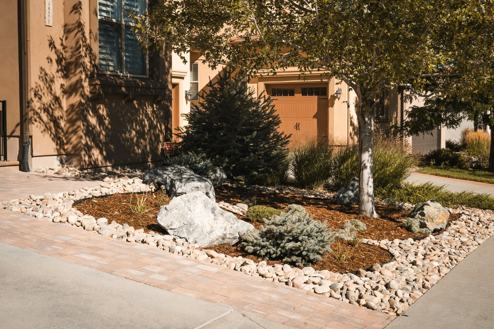 Front yard landscaping with decorative rock, trees, shrubs, and paver walkway