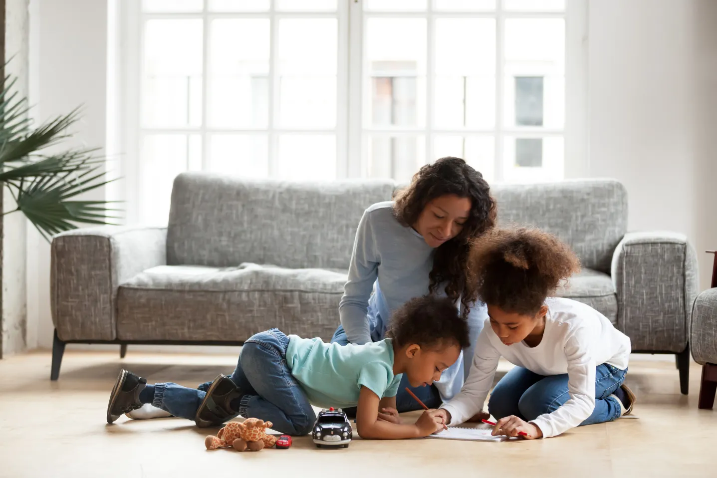 Mother and two children drawing on paper on the floor in a bright living room.