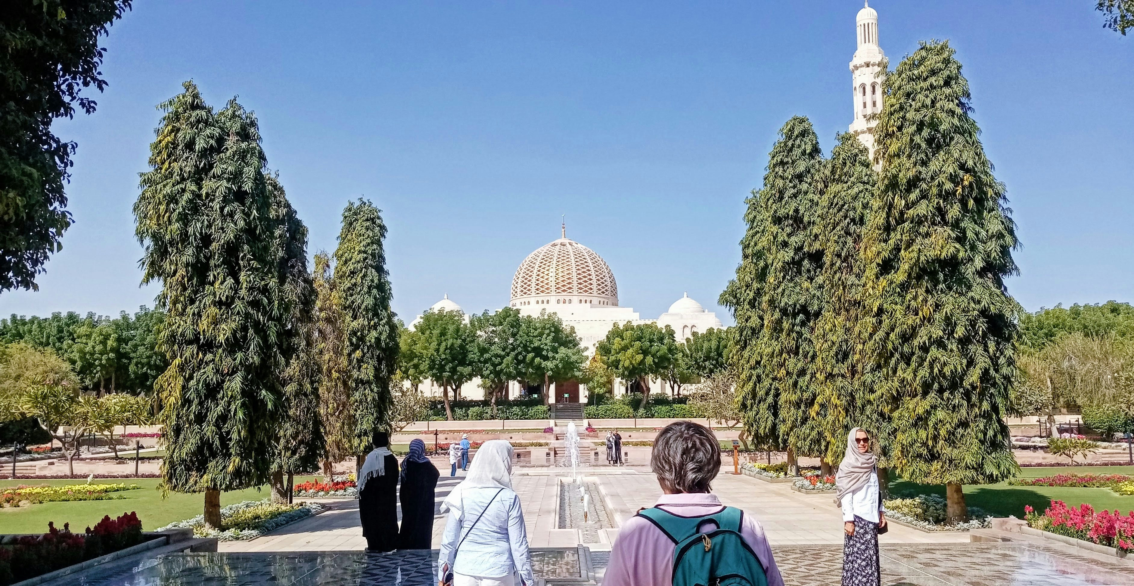 The entrance to the Sultan Qaboos Grand Mosque in Muscat, Oman, with its blue dome and visitors in the foreground