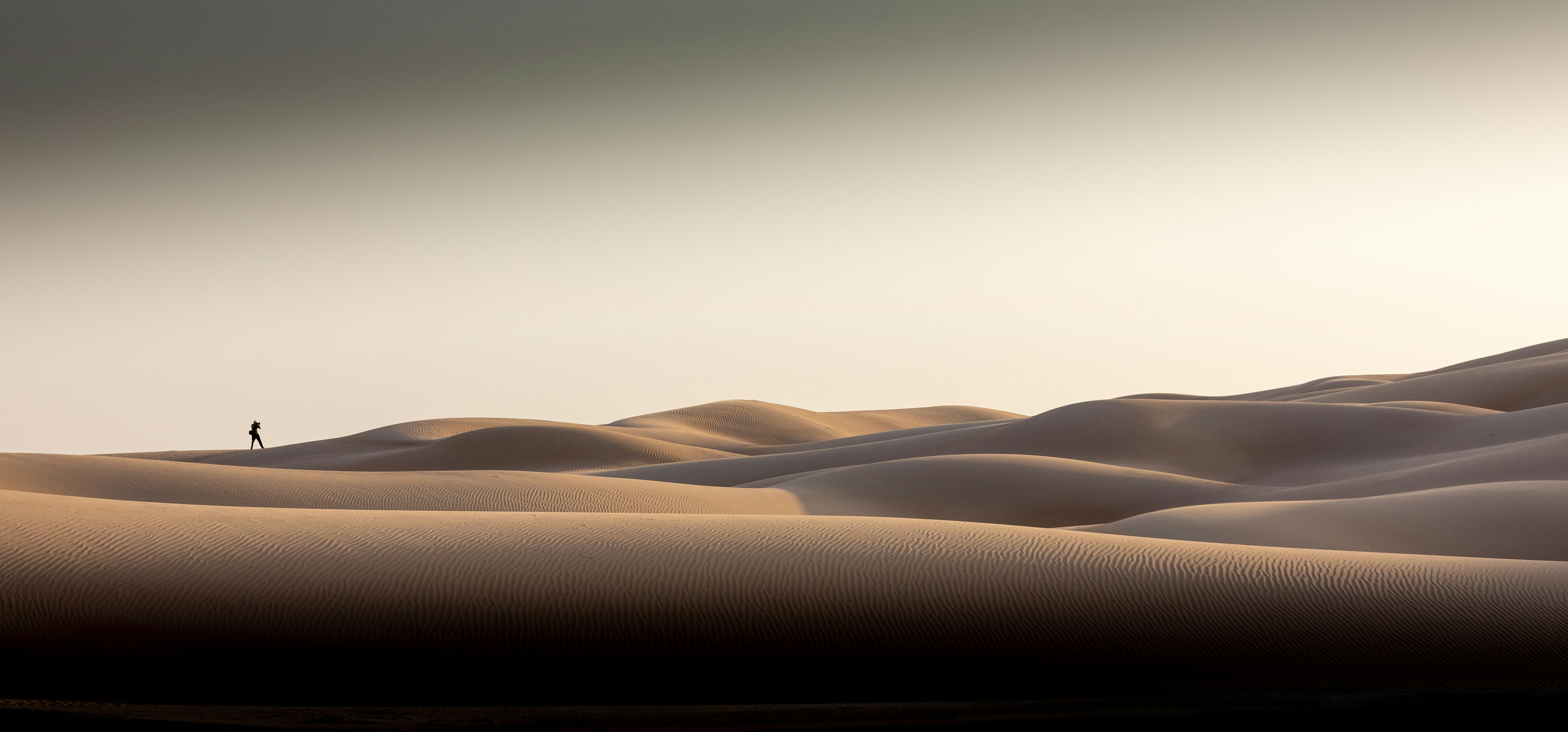 A lone figure walking across rolling desert dunes at sunset in Oman