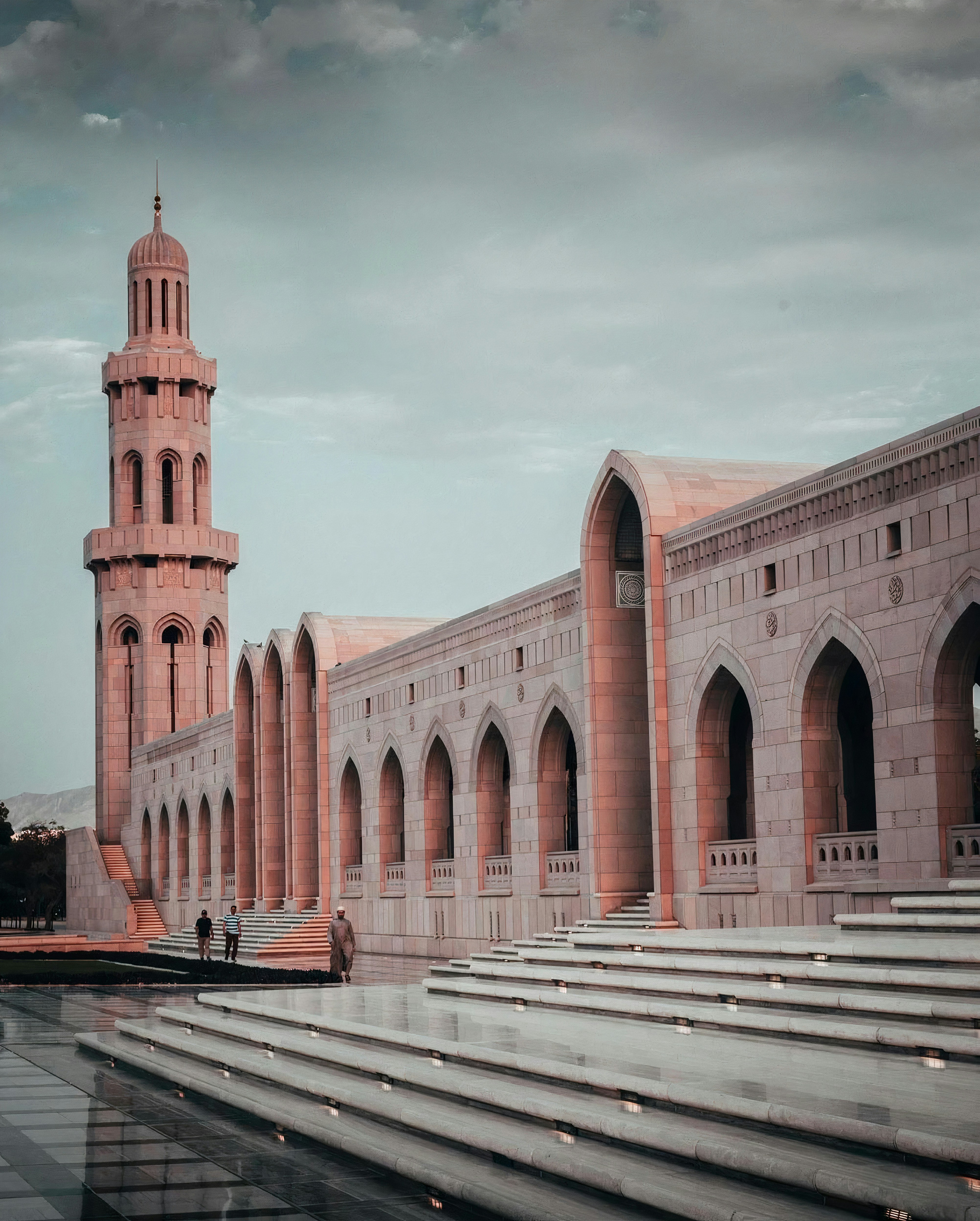 The Sultan Qaboos Grand Mosque in Muscat, Oman, with its clock tower and dome under a cloudy sky