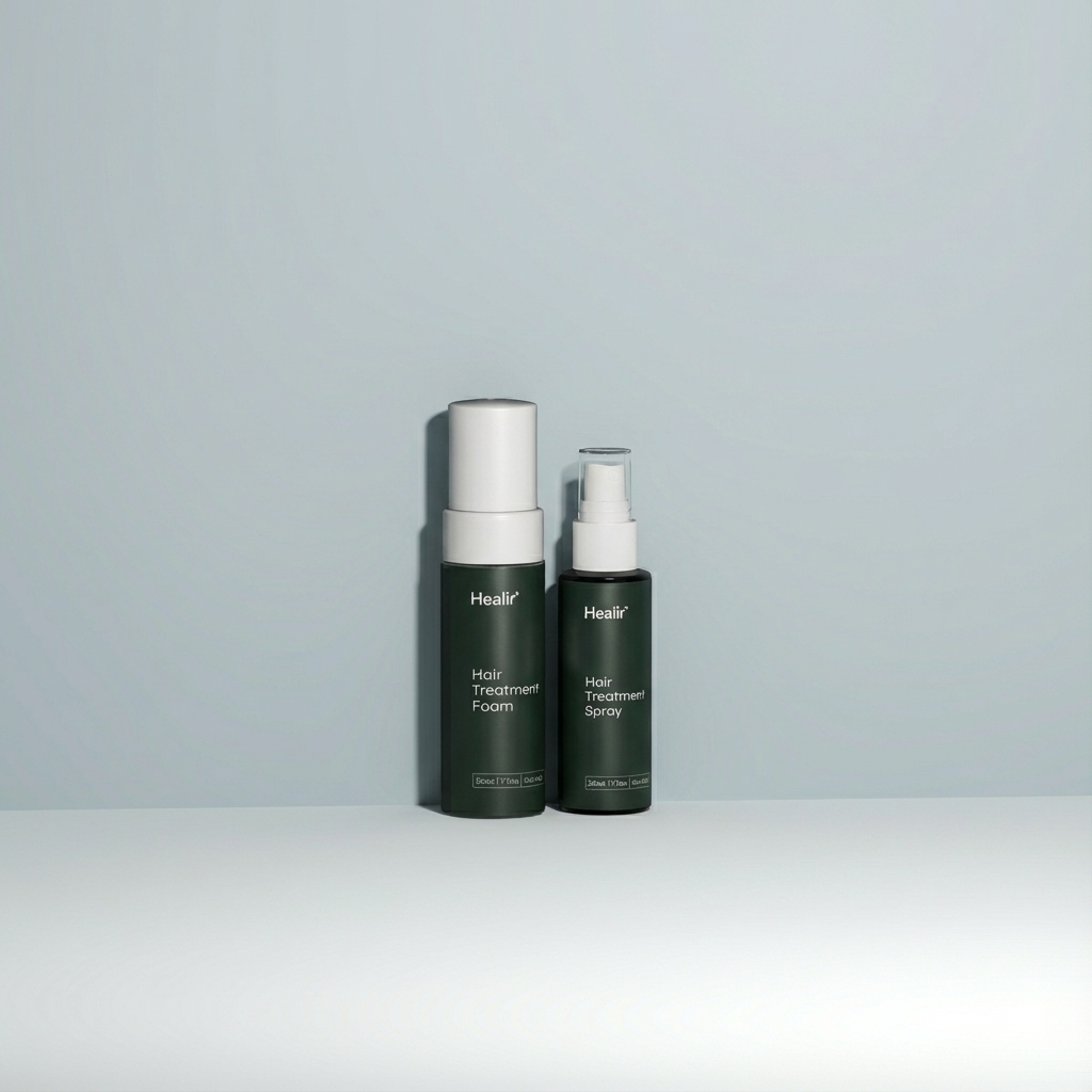 Two dark green bottles of Healiir hair treatment products on a light gray surface and background, one labeled Hair Treatment Foam and the other Hair Treatment Spray.