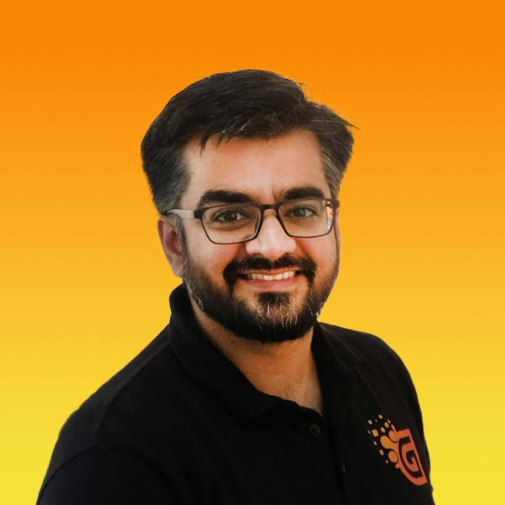 Smiling man with glasses and beard wearing a black shirt against an orange-yellow gradient background.