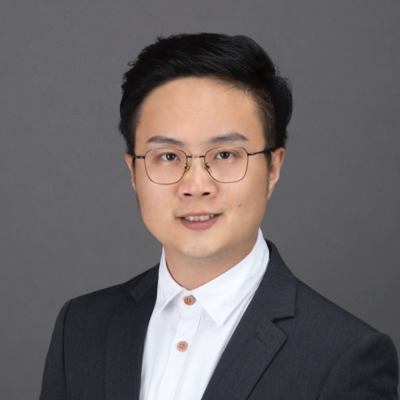 Portrait of a smiling man with glasses wearing a dark suit jacket and white collared shirt.
