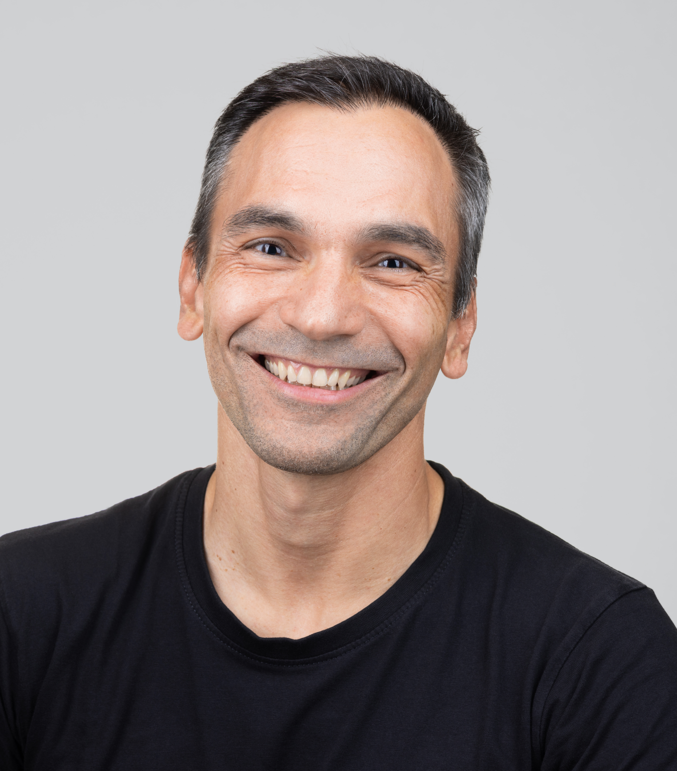 Smiling middle-aged man with short dark hair wearing a black shirt against a gray background.